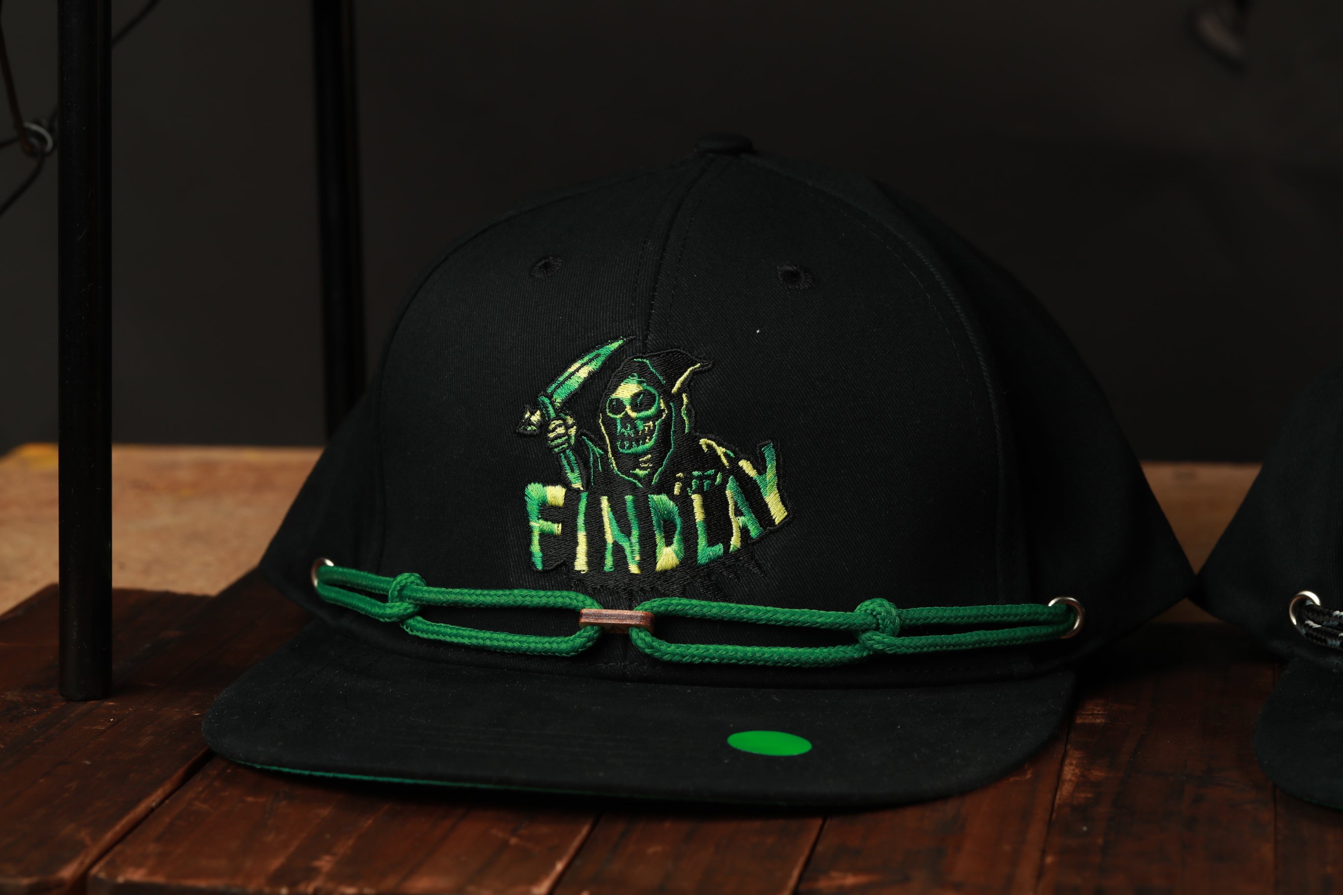 A black baseball cap with a green band and a skull logo on it, placed on a wooden surface.