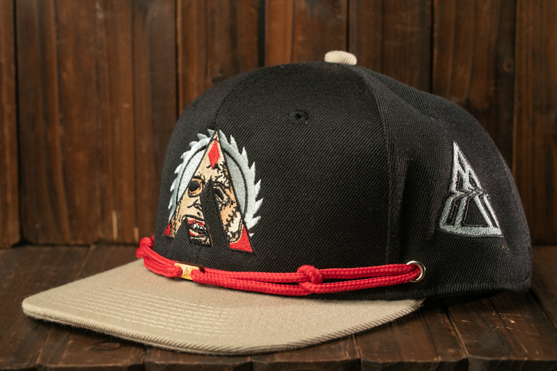 A black baseball cap with a red string and a graphic design on the front, placed on a wooden surface.