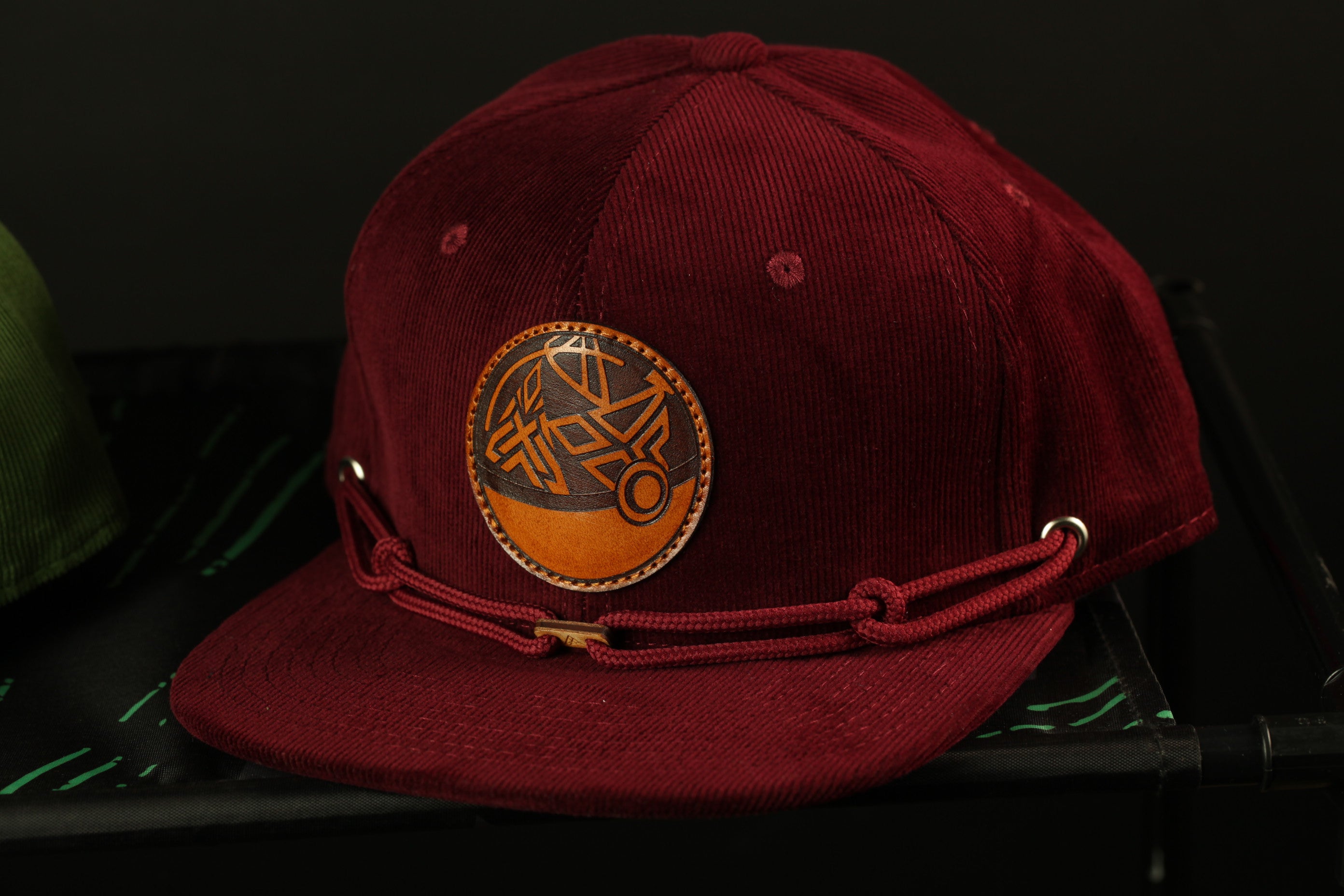 A burgundy baseball cap with a circular logo on the front, sitting on a black surface.
