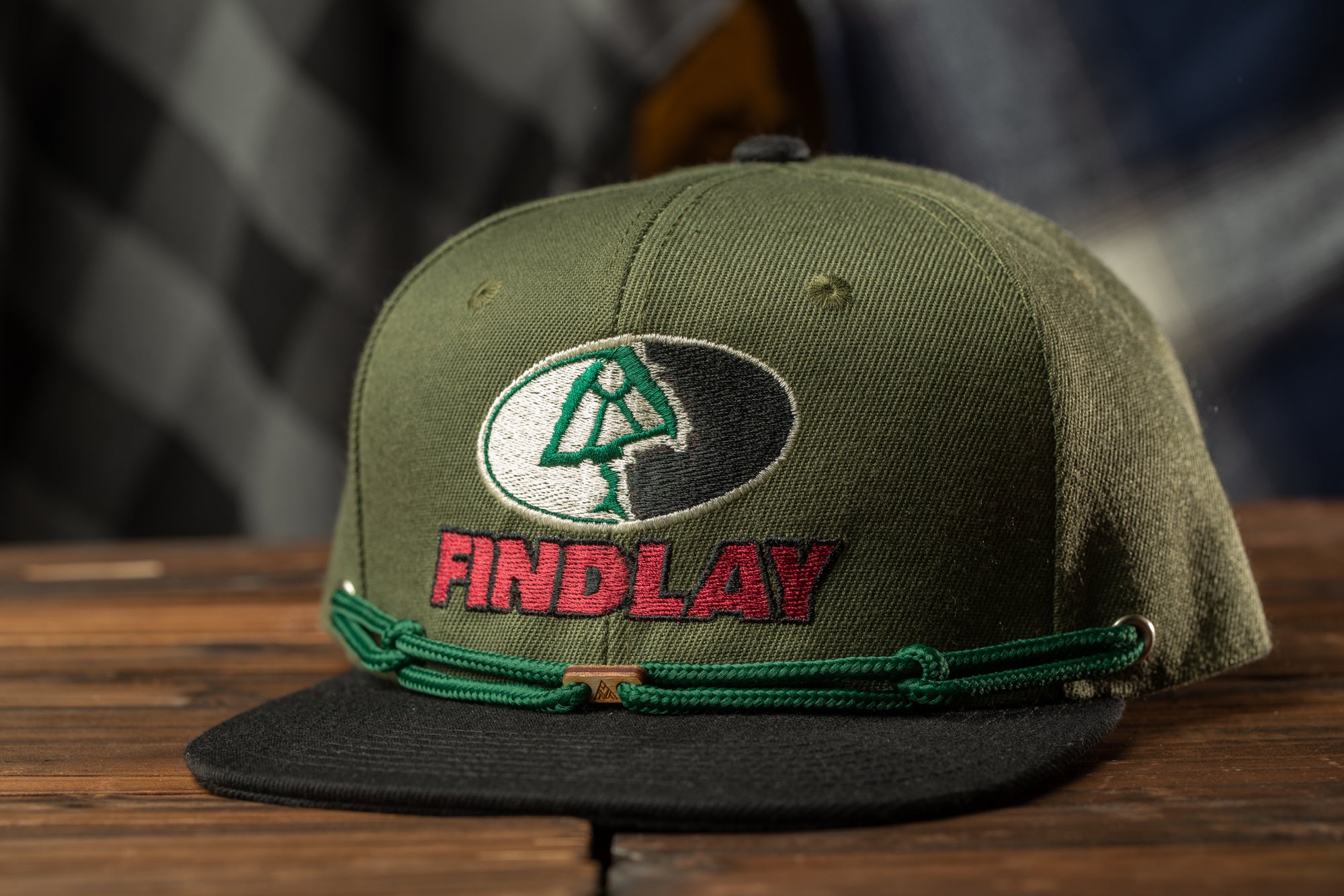 A green baseball cap with the word "FINDLAY" printed on it, sitting on a wooden surface.