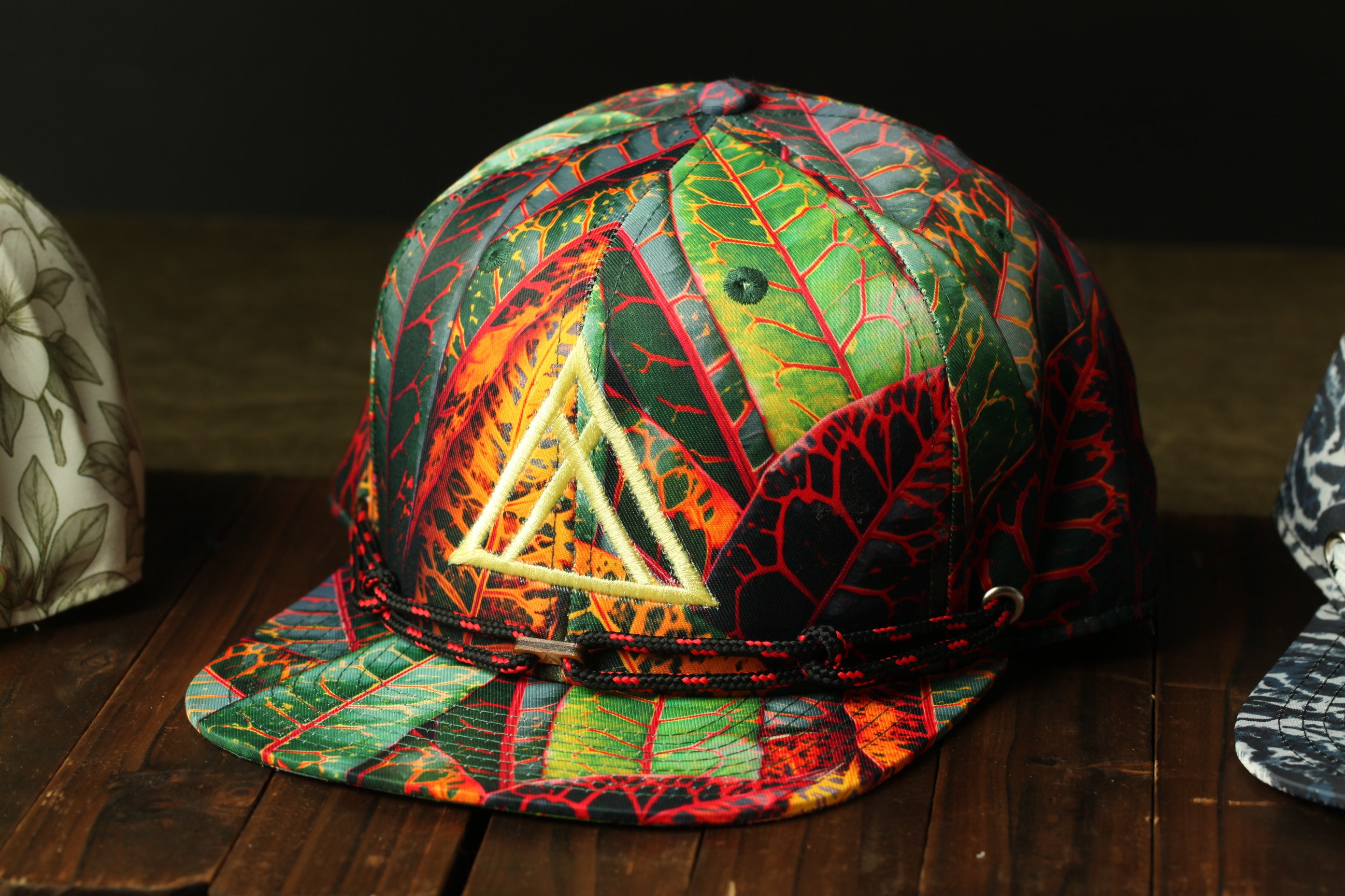 A colorful, patterned baseball cap with a leaf design sits on a wooden surface.