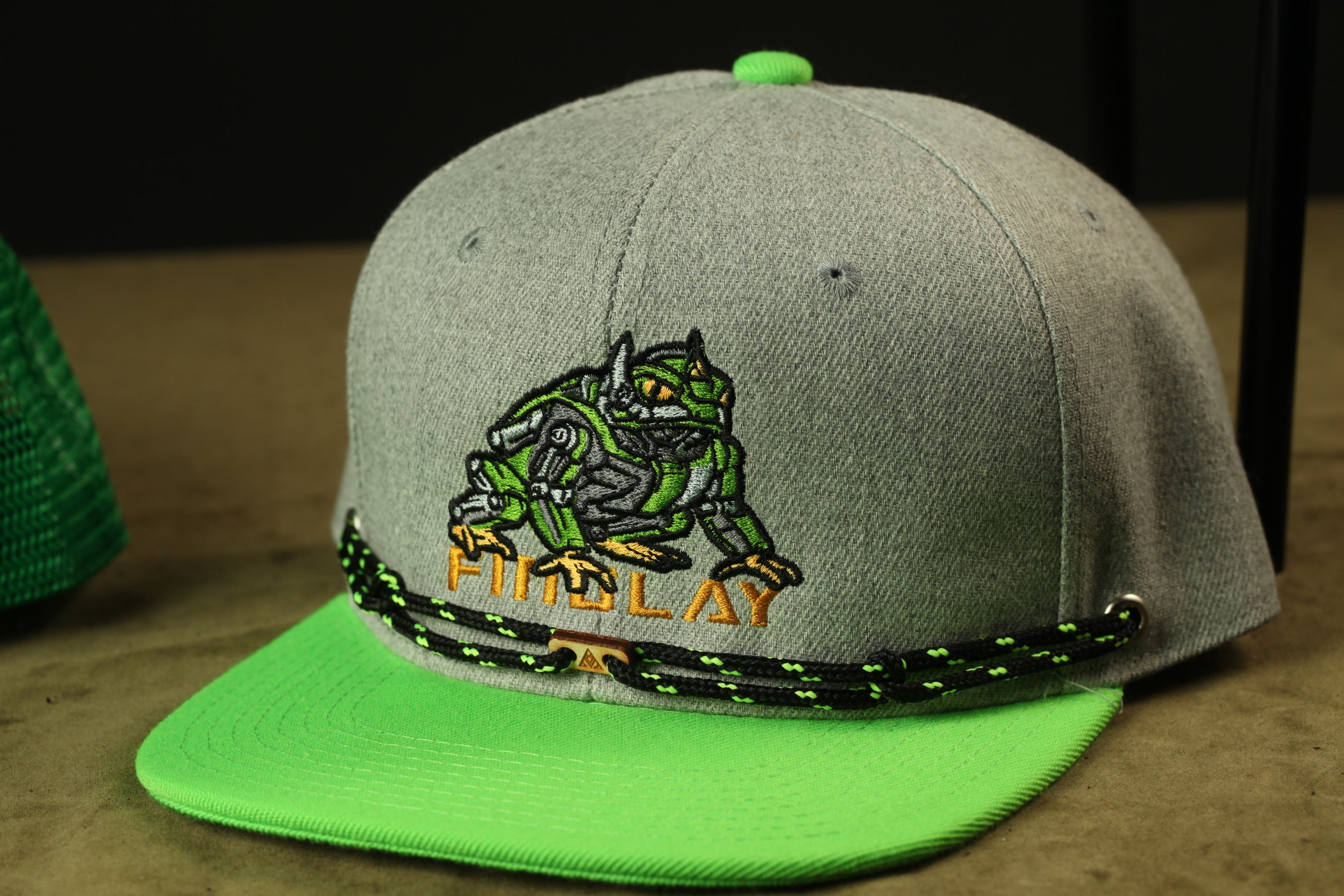 A grey baseball cap with a green brim and a green and black string around the brim.