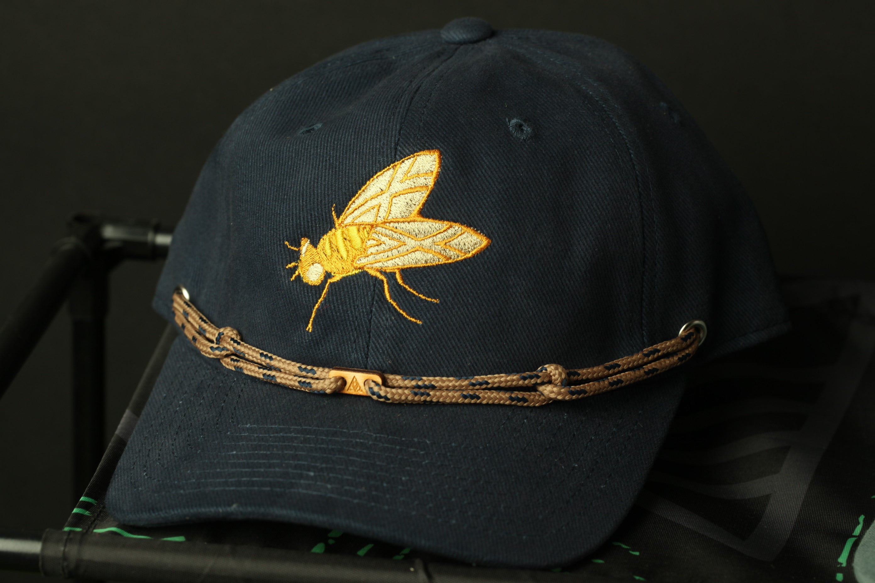 A black baseball cap with a yellow embroidered design of a fly on the front.