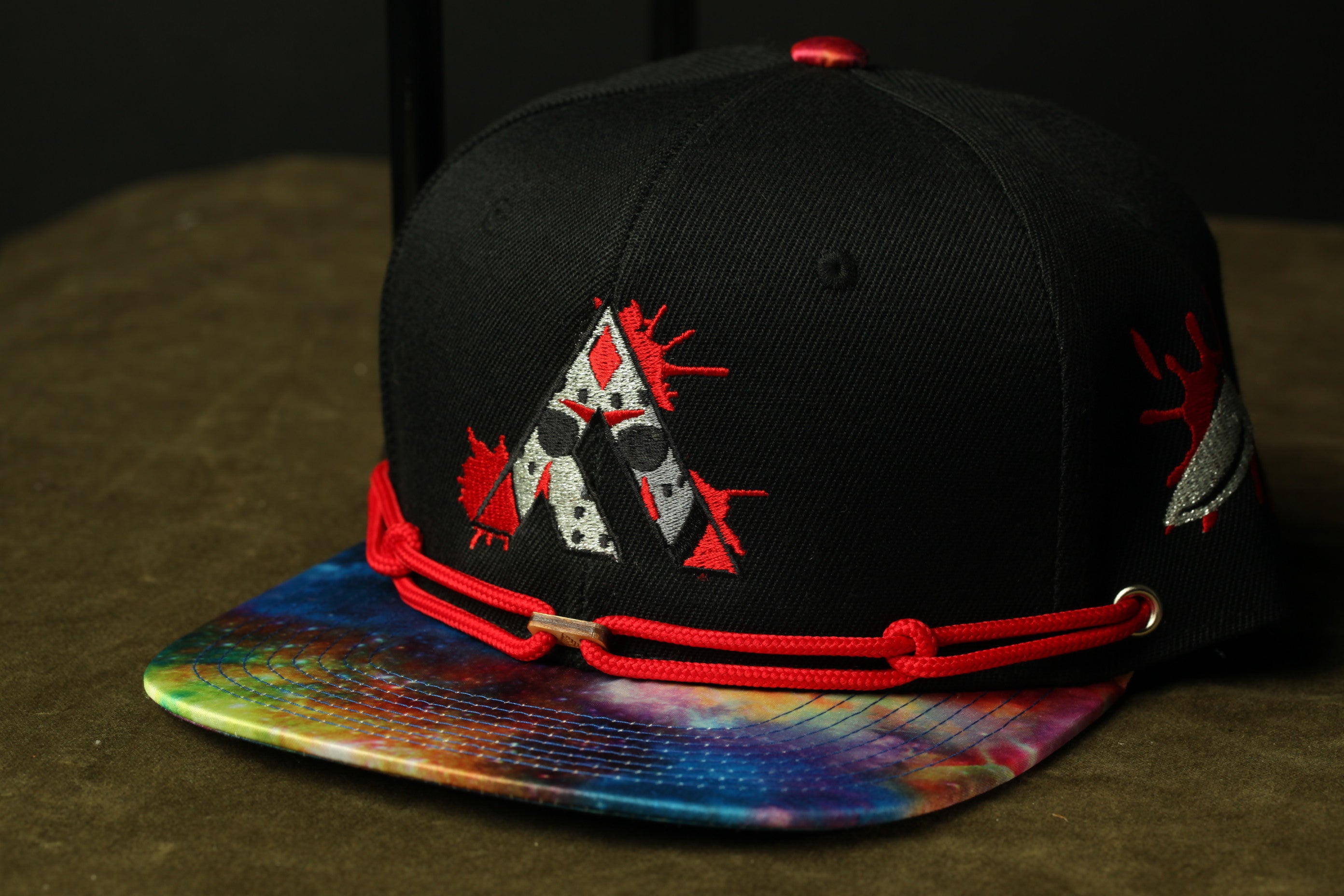 A black baseball cap with a tie-dye pattern and a red string around the brim.