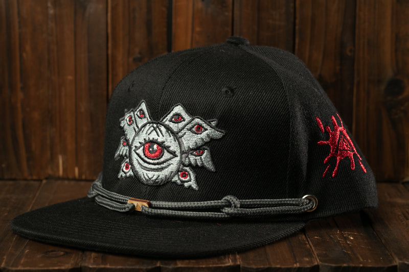 A black baseball cap with a unique design featuring a large eye and a red spider-like element on the side.