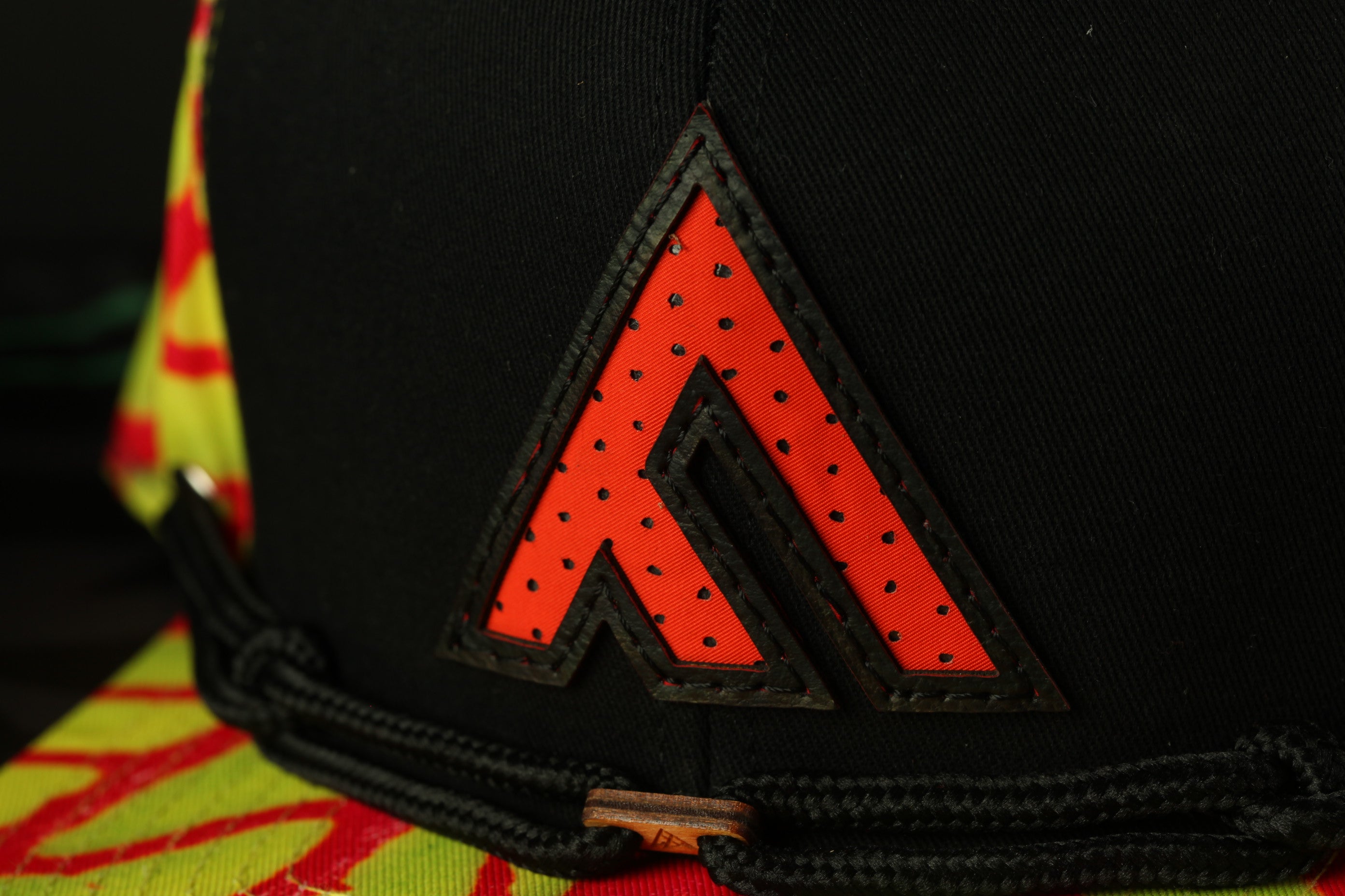 A close-up view of a black baseball cap with a red and yellow patterned fabric and a large red triangle logo on the front.