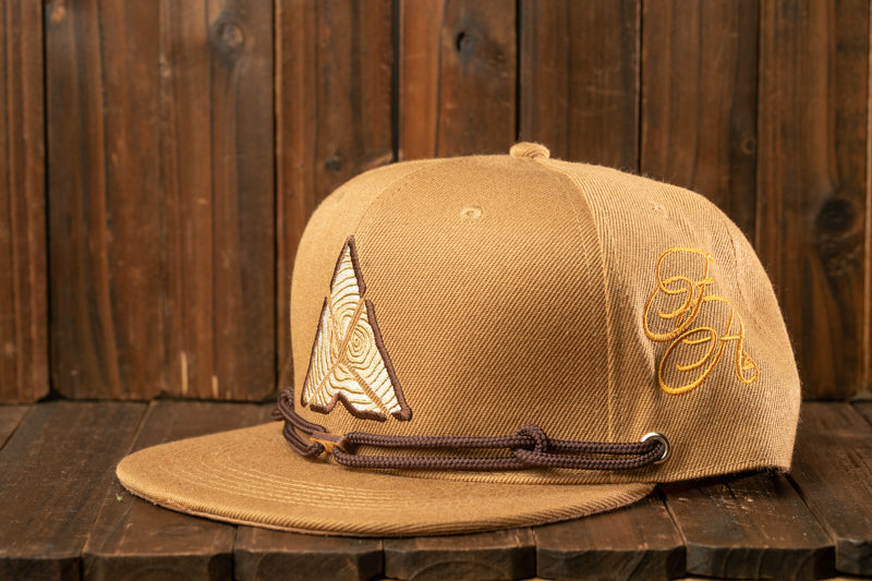 A tan baseball cap with a brown leather strap and a unique logo on the front, placed on a wooden surface.