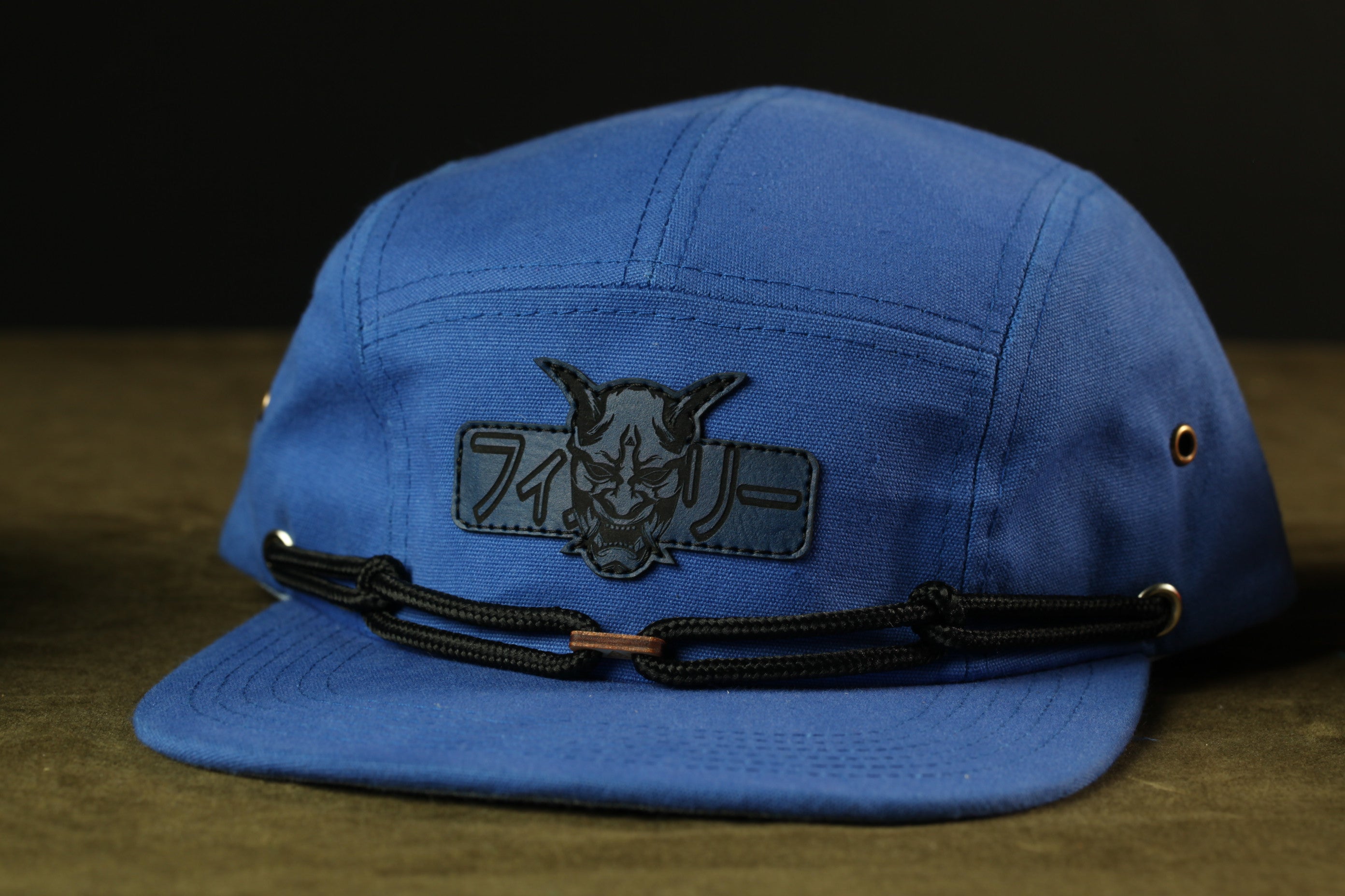 A blue baseball cap with a black patch featuring a graphic design.