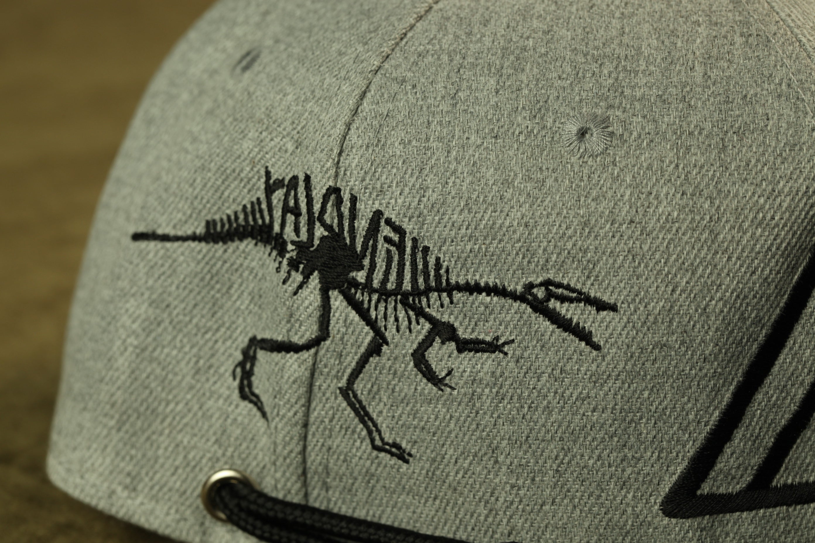 a grey baseball cap with a black dinosaur skeleton embroidered on it.