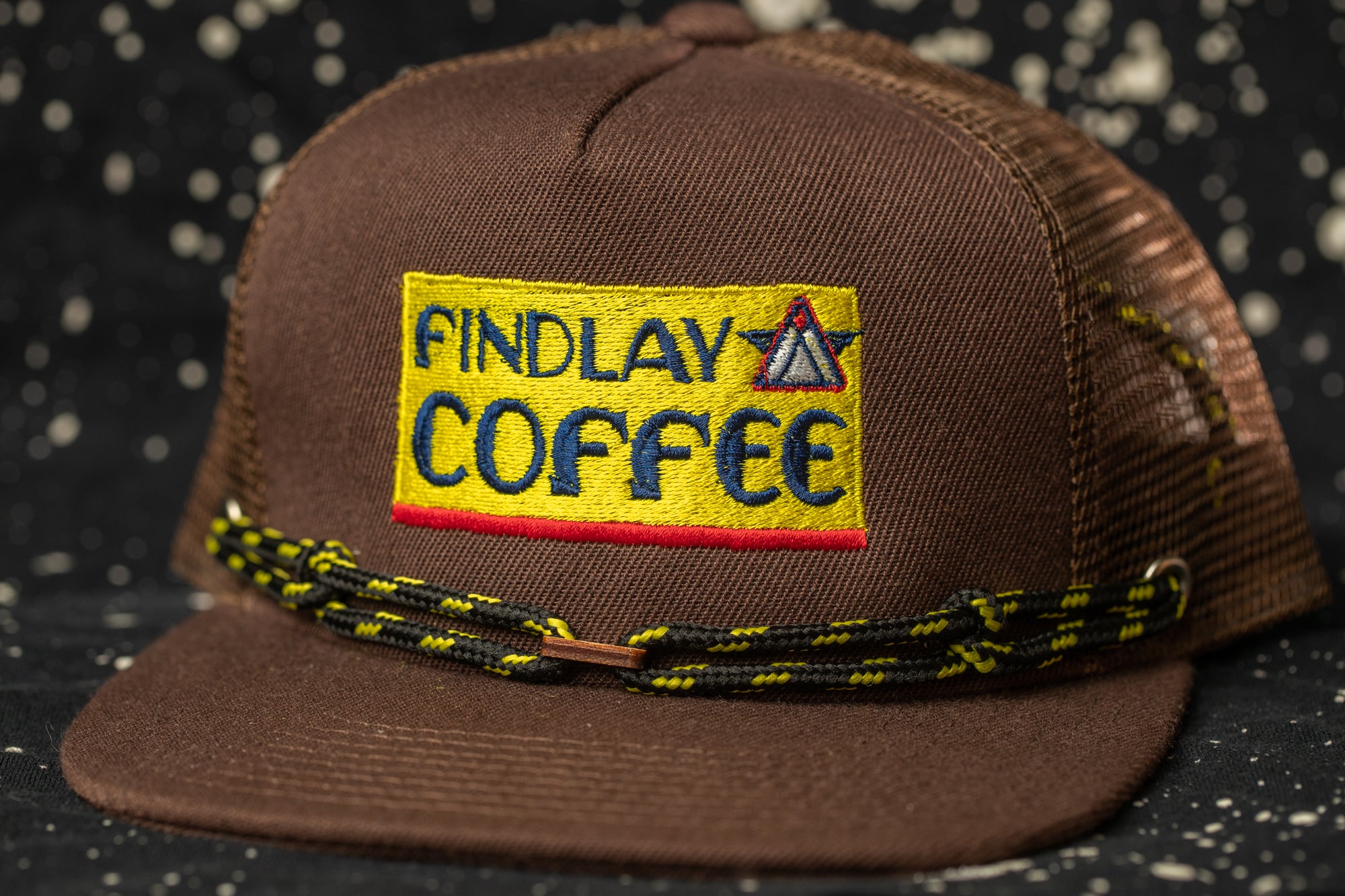 A brown baseball cap with a yellow patch that says "Findlay Coffee".