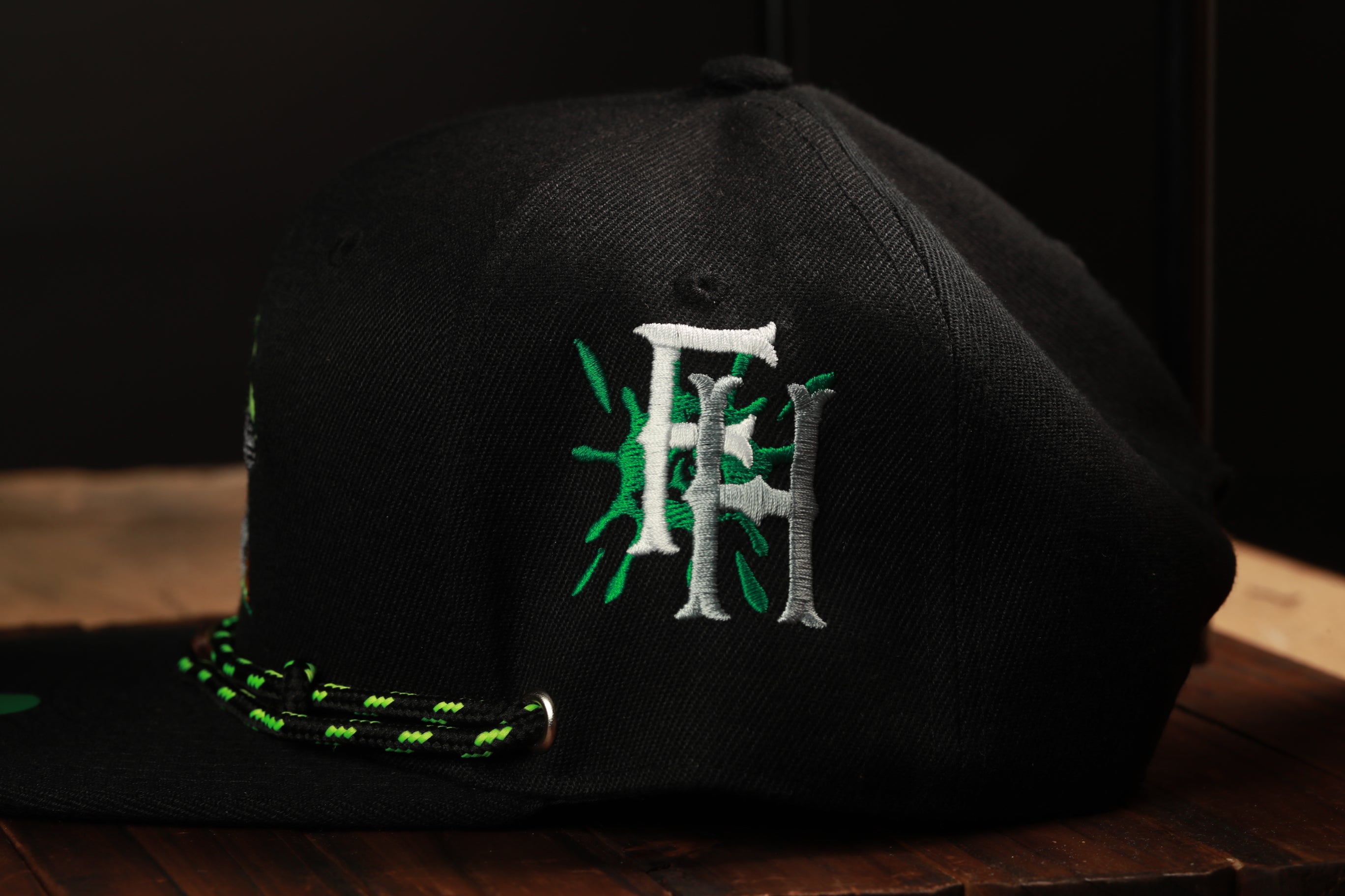 A black baseball cap with a green and white embroidered logo on the side.