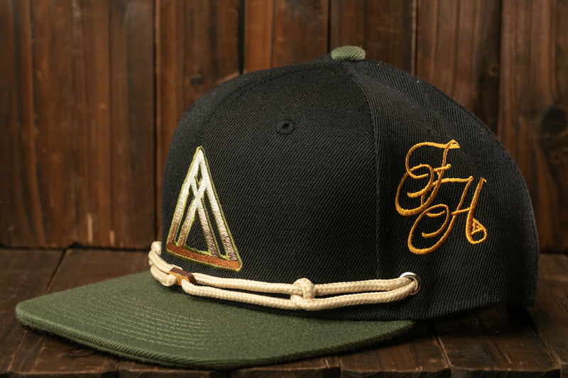 A black baseball cap with a green brim and a gold-colored logo on the front, placed on a wooden surface.