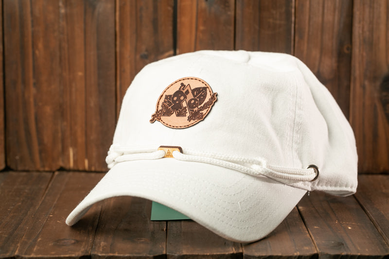 A white baseball cap with a leather patch featuring a cartoon character is displayed on a wooden surface.