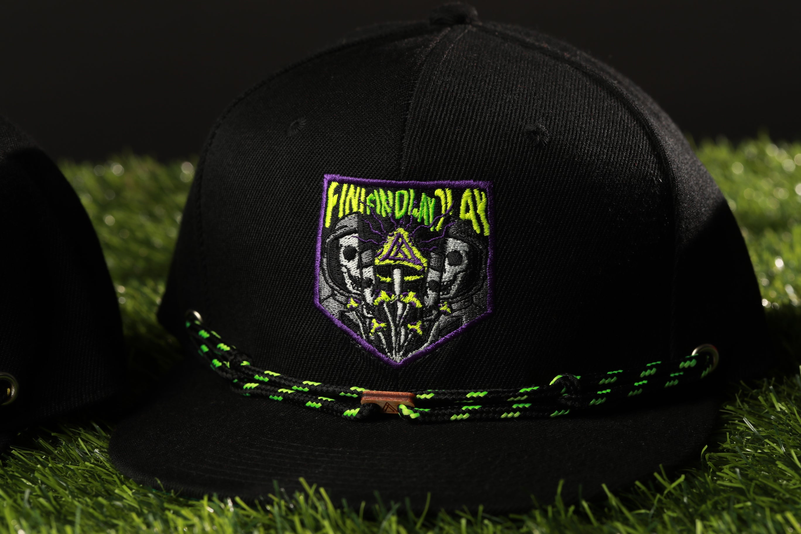 A black baseball cap with a green and yellow embroidered logo on the front, placed on a grassy surface.