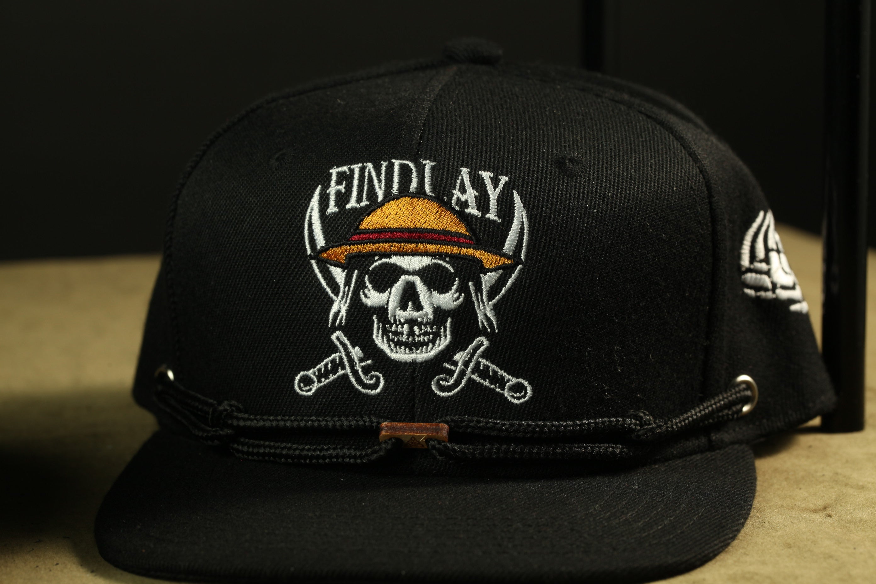 A black baseball cap with a skull and crossed swords design, along with the text "FINDUY" printed on it.