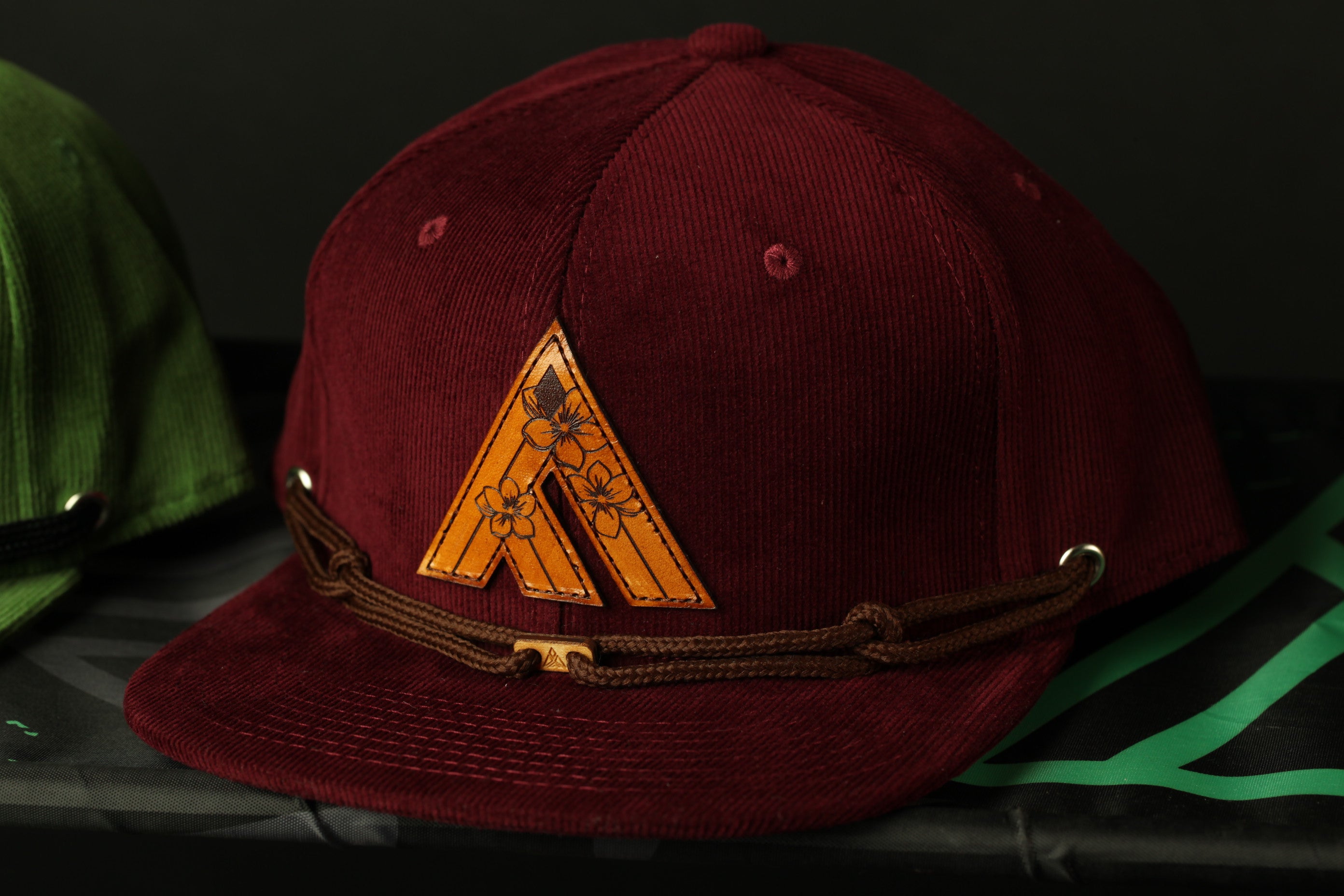 A burgundy baseball cap with a brown leather logo on the front, placed on a black surface.