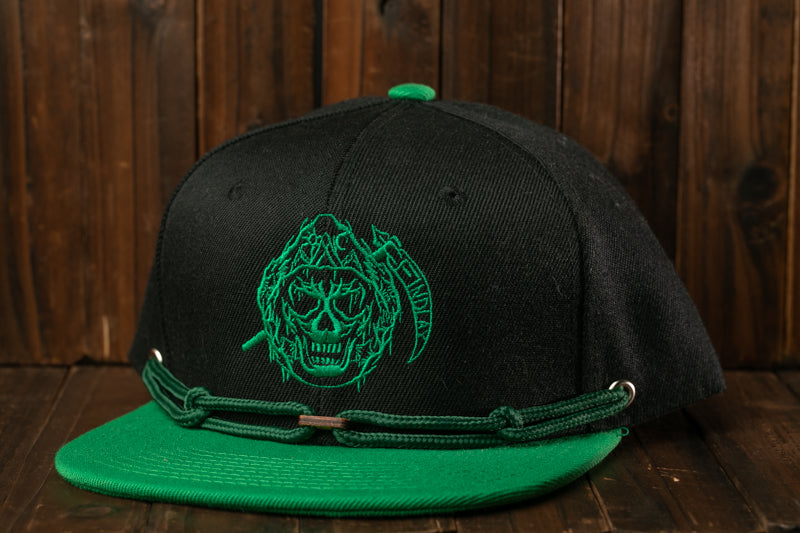 A black baseball cap with a green skull design on the front, placed on a wooden surface.