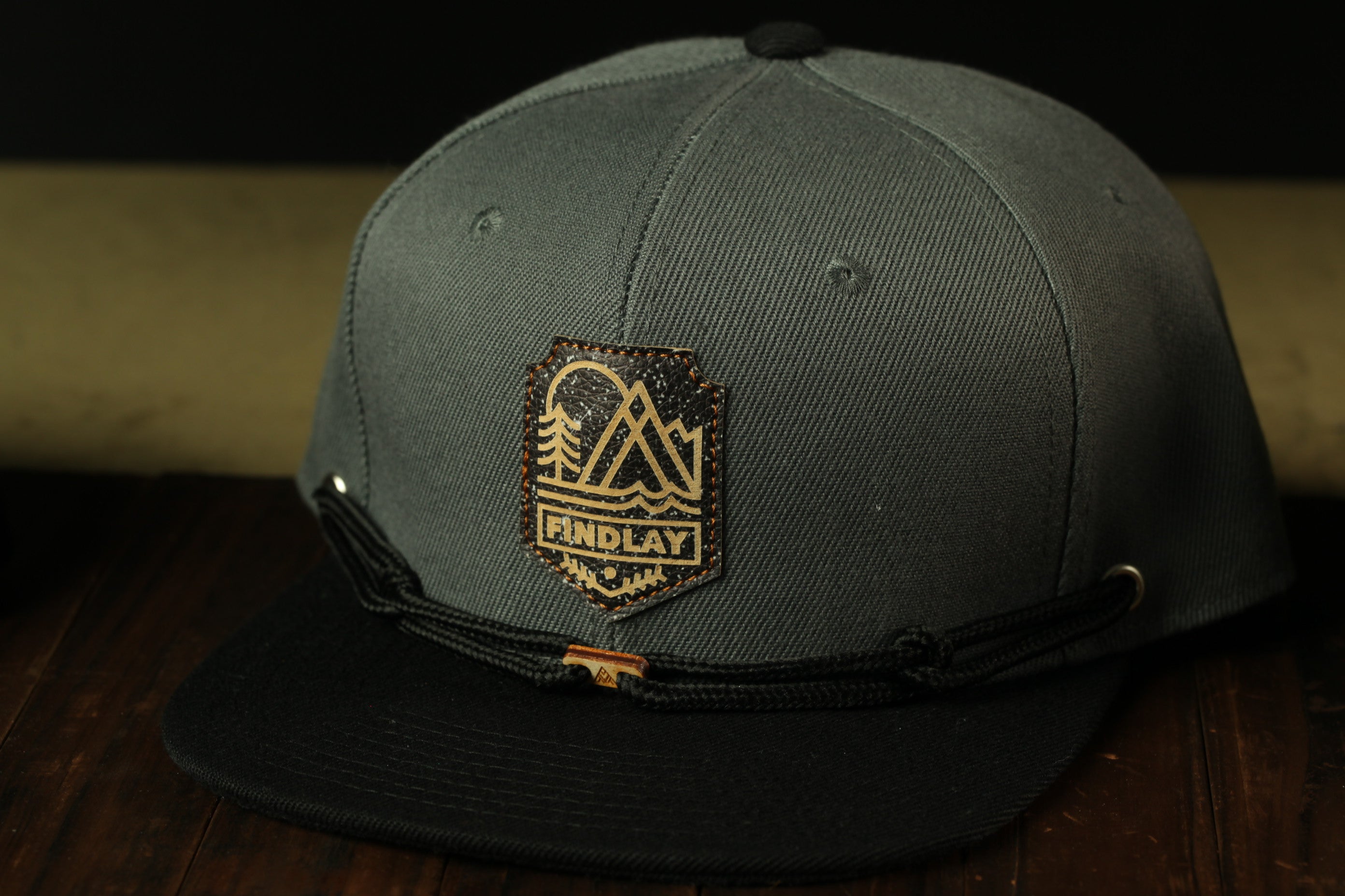 A gray baseball cap with a black brim and a black band around the front. The cap has a logo on the front, which appears to be a mountain or landscape design.