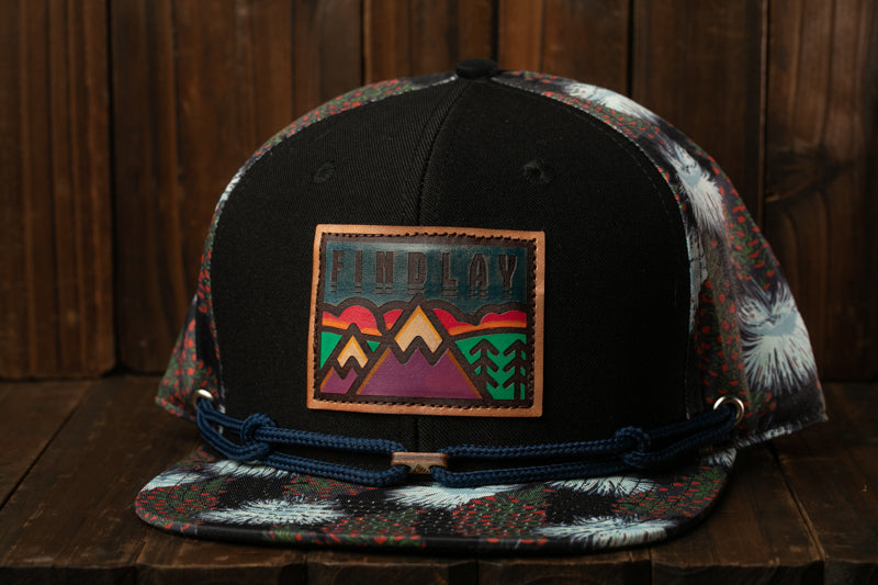 A black baseball cap with a colorful patch on the front, featuring a mountain landscape design.