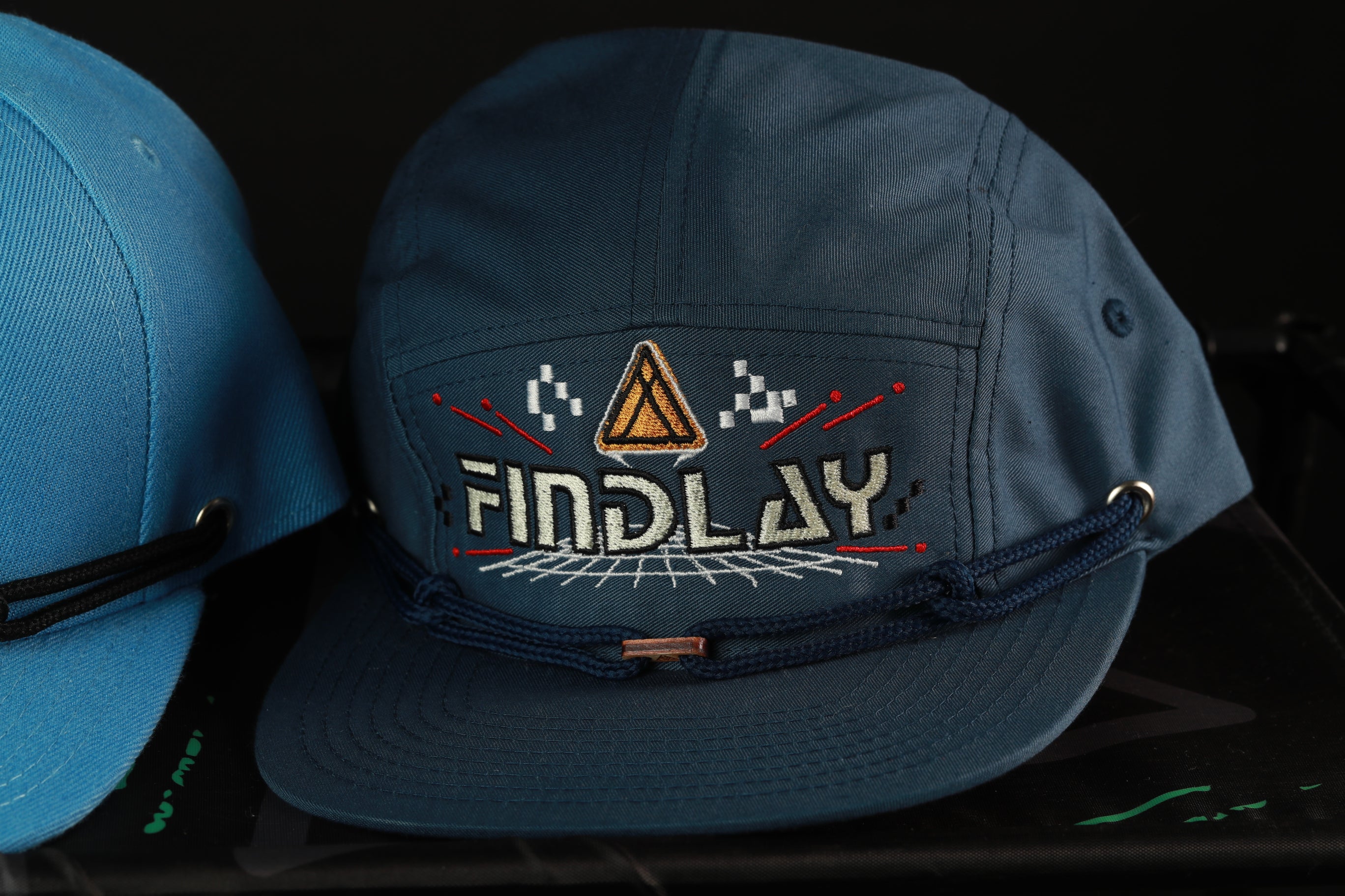 A blue baseball cap with the word "FINDLAY" printed on it, along with a graphic design.