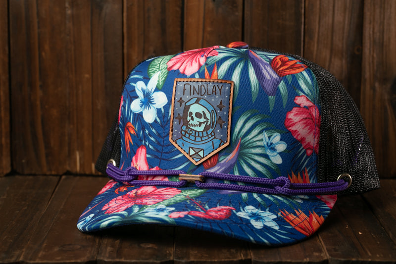 A colorful baseball cap with a floral pattern and a skull patch, sitting on a wooden surface.