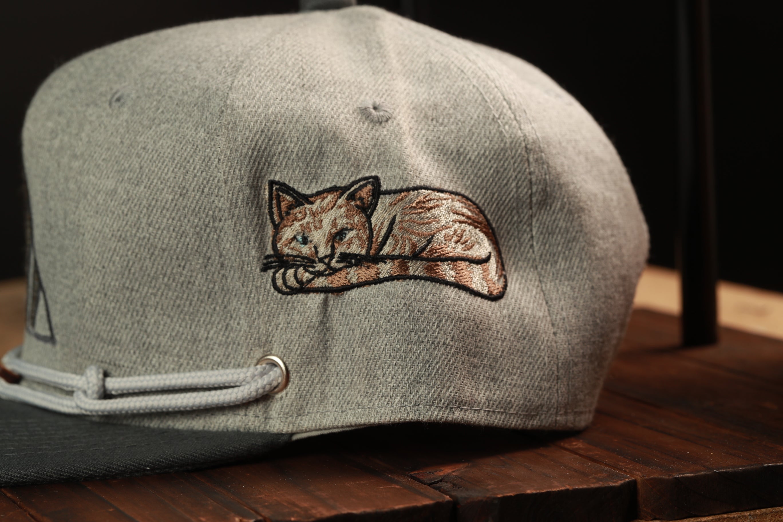 A gray baseball cap with a cat embroidered on the front, resting on a wooden surface.