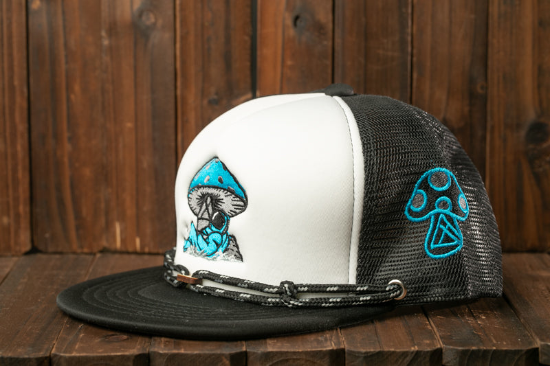 A black and white baseball cap with a mushroom design on the front and a blue mushroom design on the side, sitting on a wooden surface.
