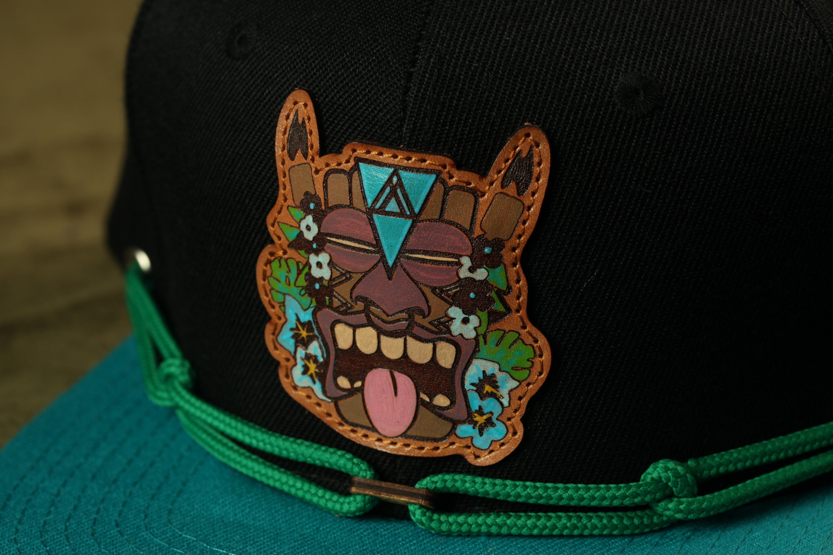 A close-up view of a black baseball cap with a colorful, cartoonish tiki mask design on the front.