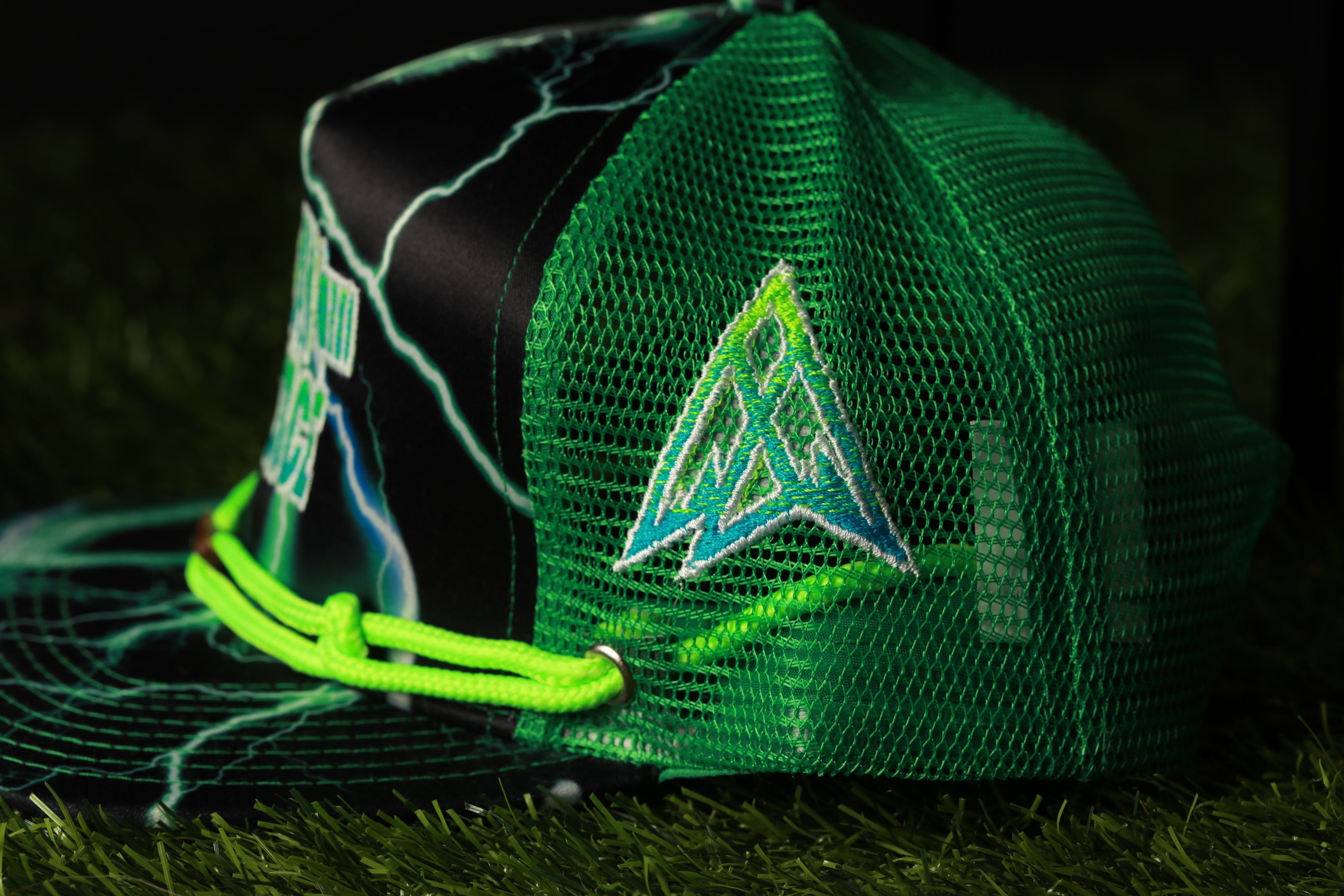 A green mesh baseball cap with a lightning bolt design and a logo on the side, resting on a grassy surface.