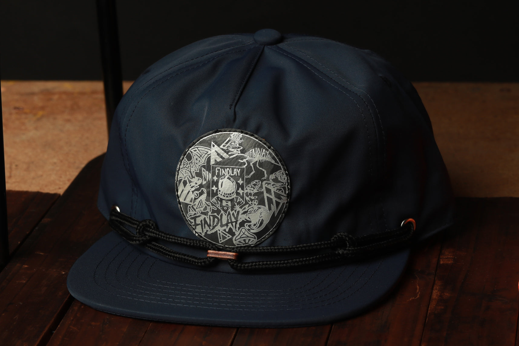 A navy blue baseball cap with a circular logo on the front, sitting on a wooden surface.