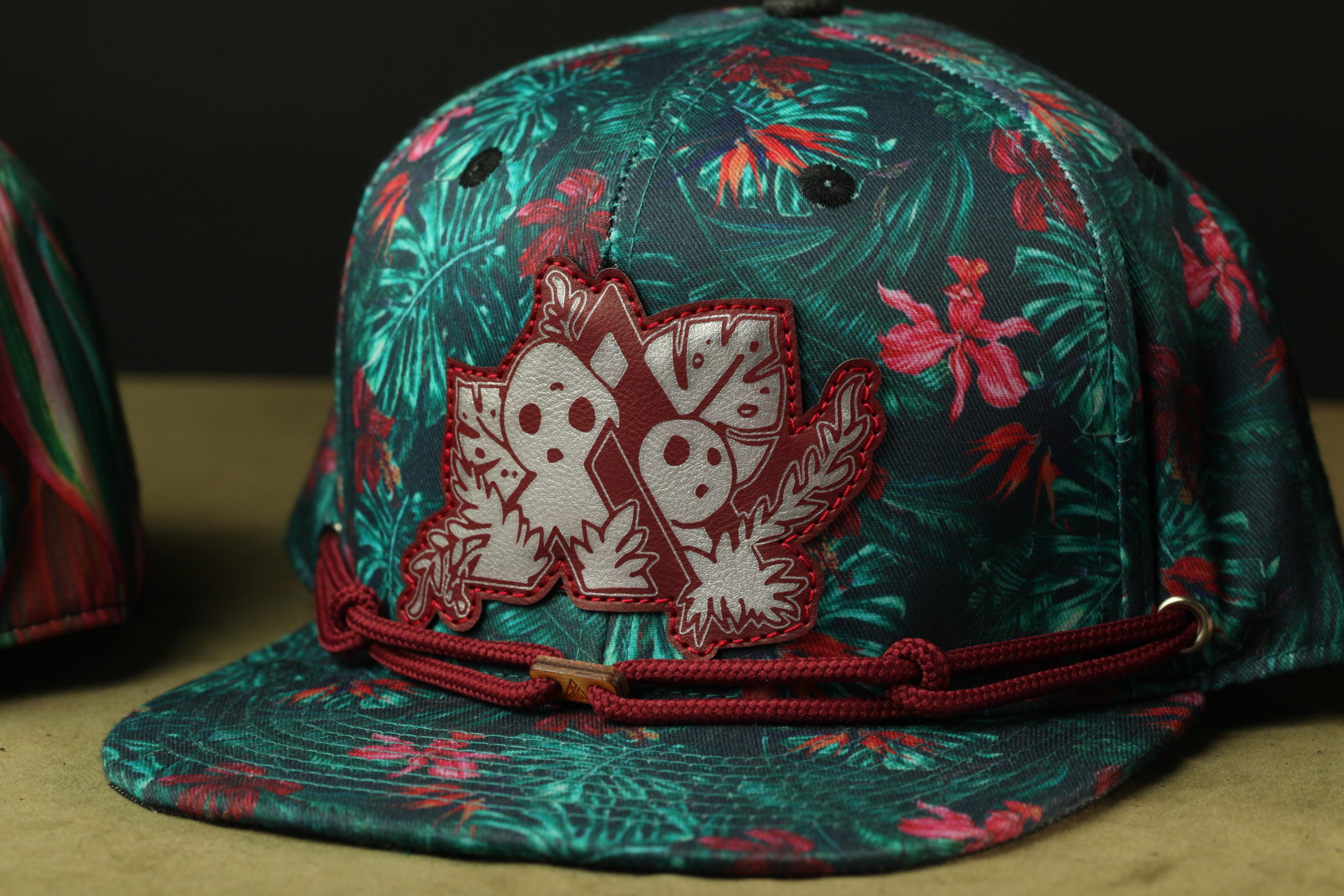 A colorful floral-patterned baseball cap with a red-colored trim and a distinctive patch design on the front.
