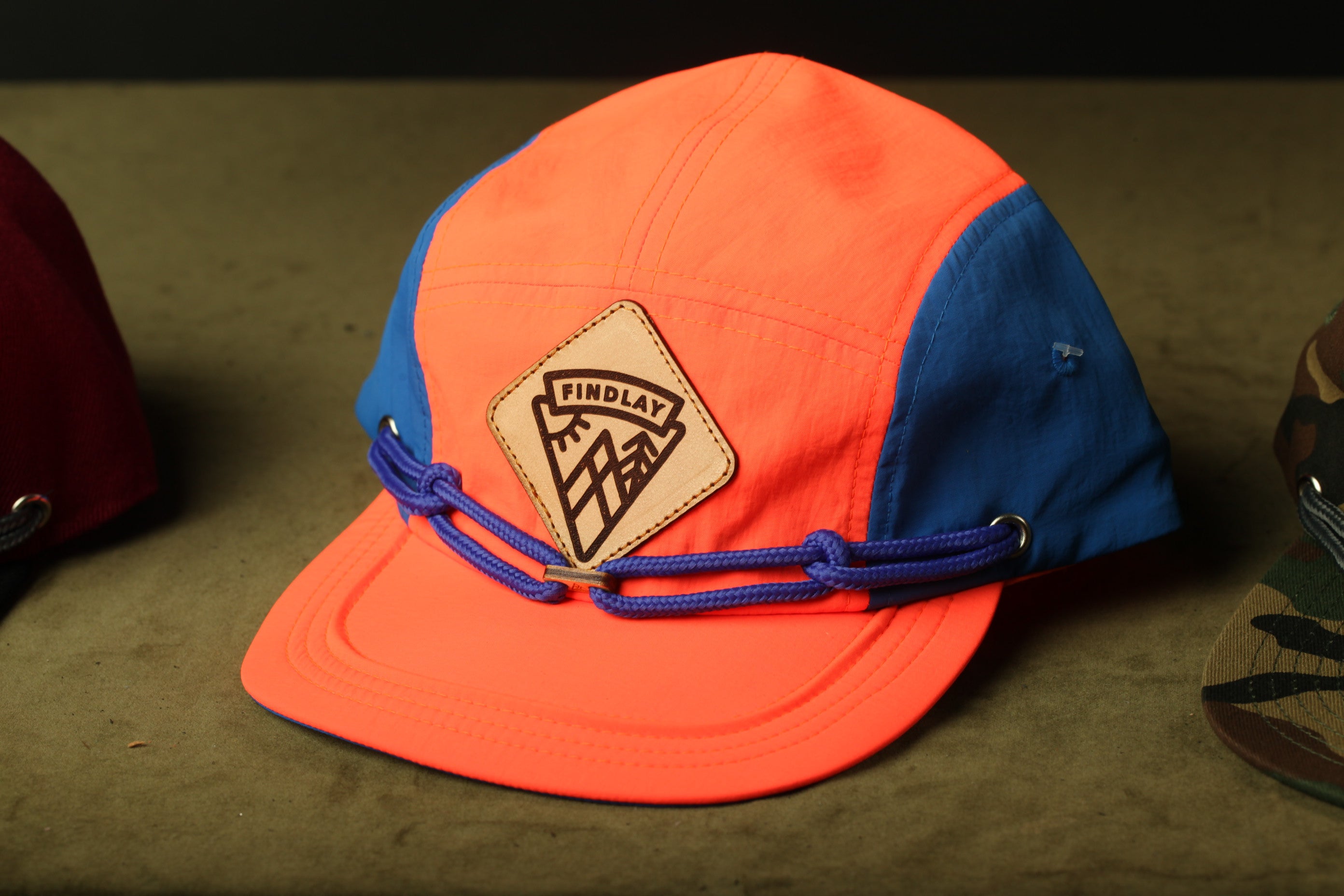 A bright orange and blue baseball cap with a leather patch on the front, sitting on a surface.