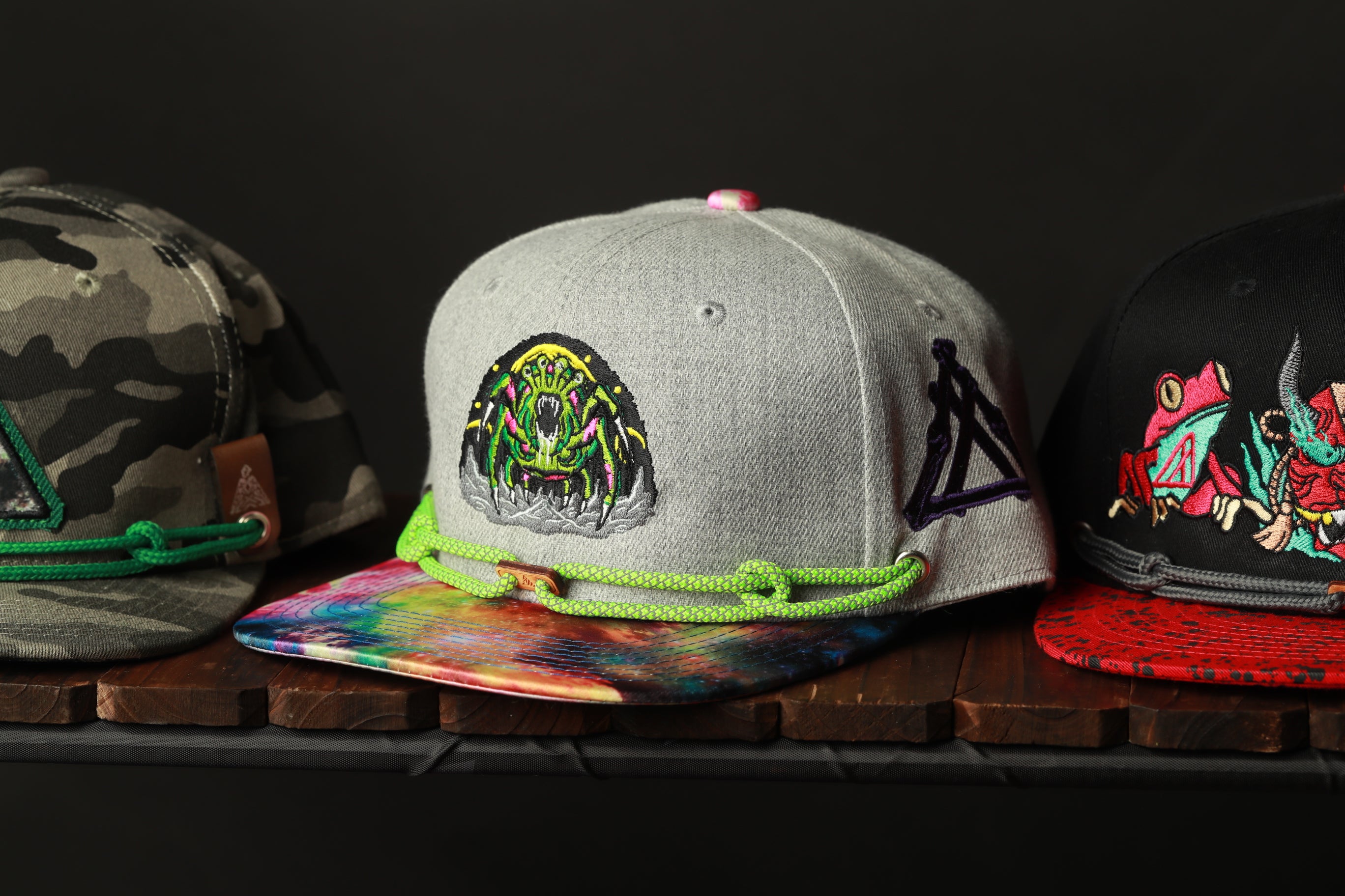 Three baseball caps with different designs and colors are displayed on a wooden surface.