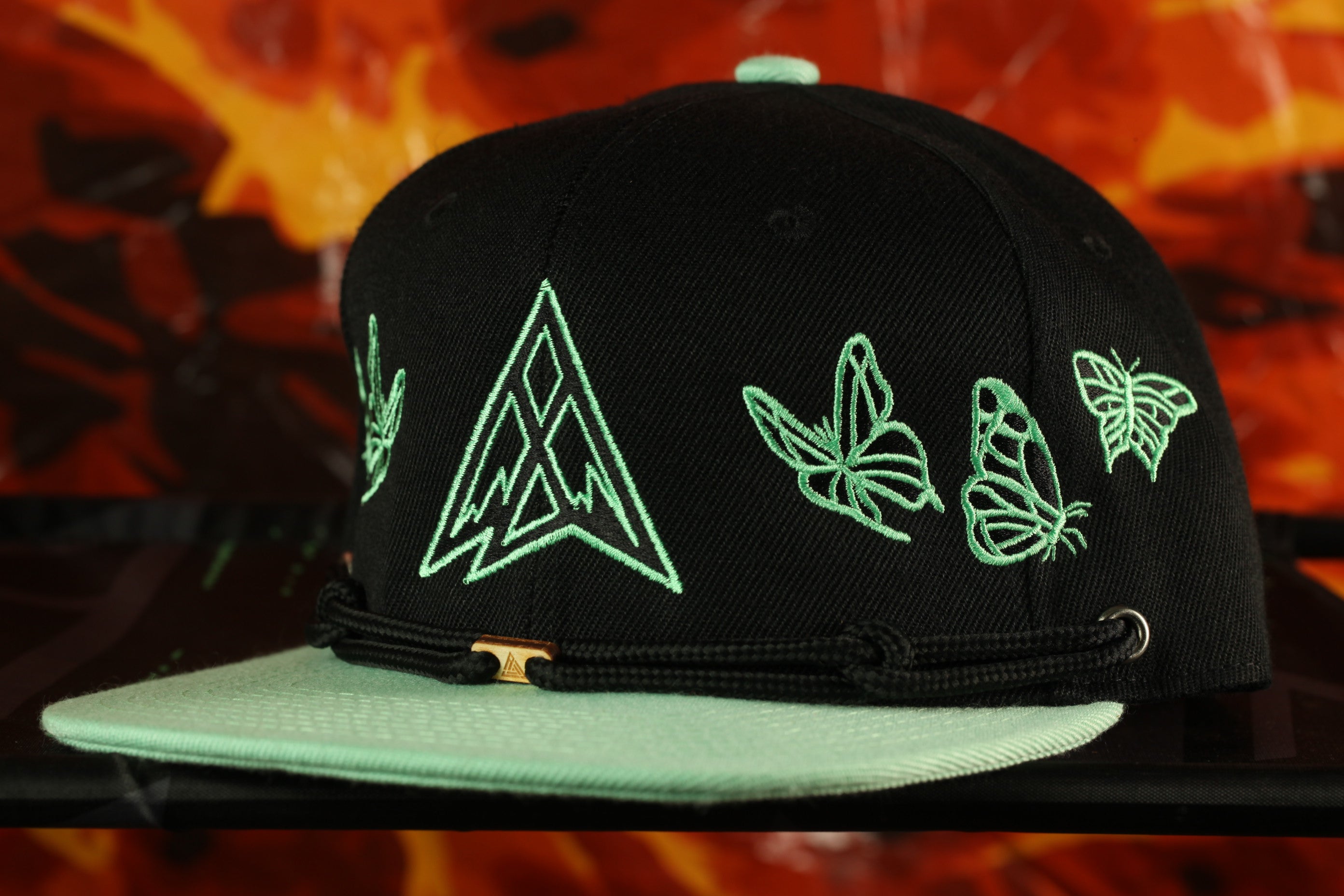 A black baseball cap with green embroidered butterflies and a triangular logo on the front.