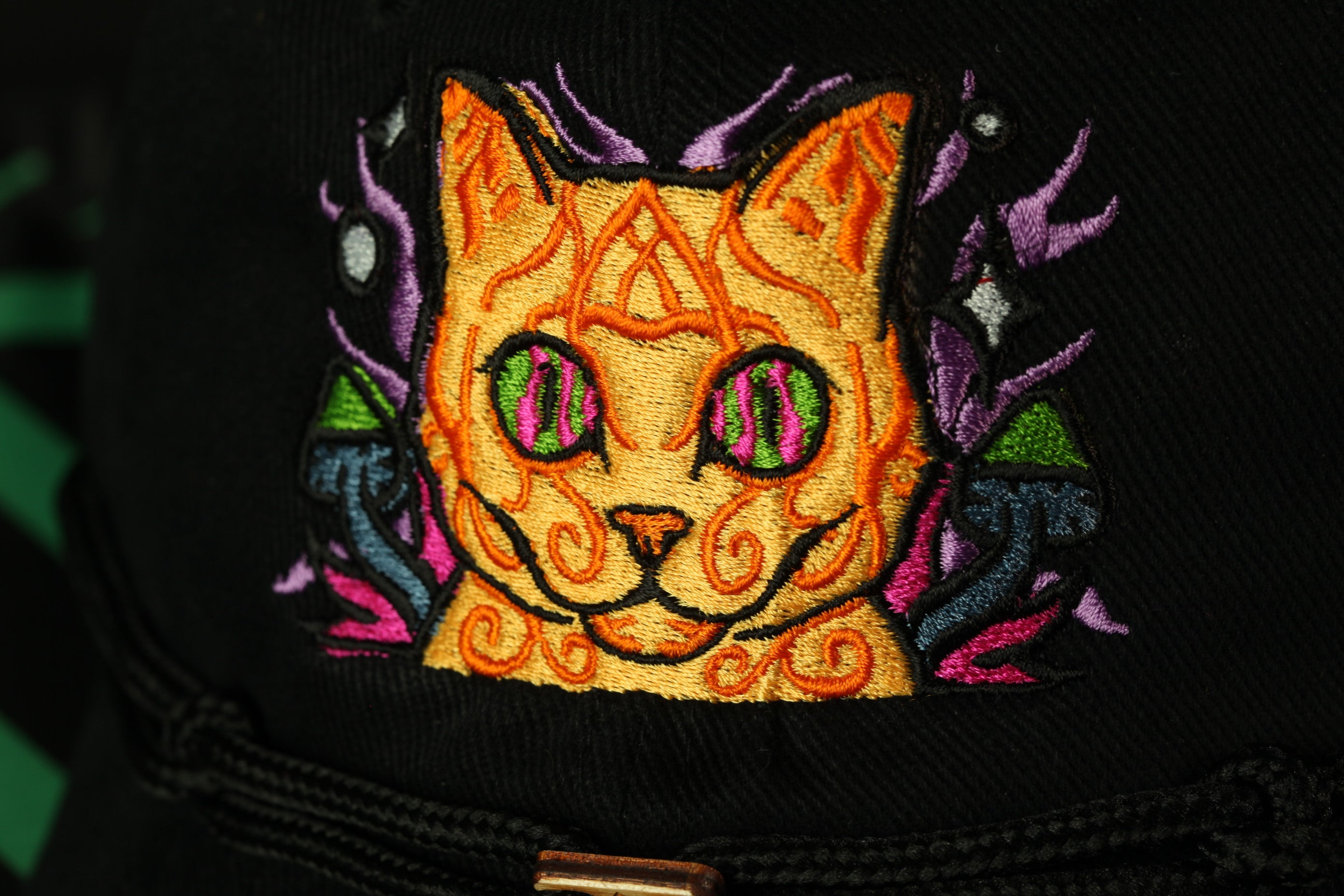 a close-up view of a colorful, embroidered cat with a yellow and orange patterned face, surrounded by purple and green elements.