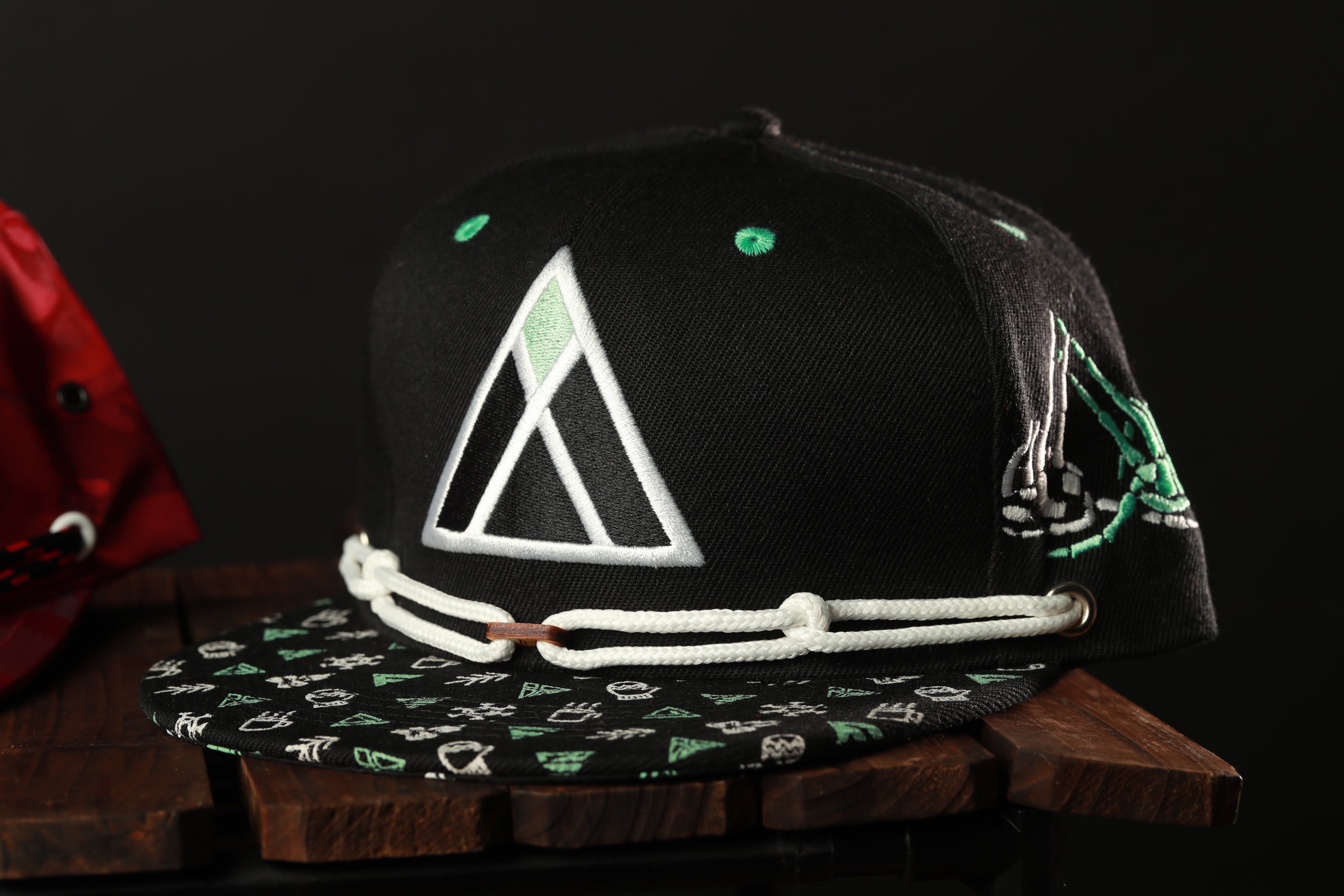 A black baseball cap with a white triangle design and green accents, placed on a wooden surface.