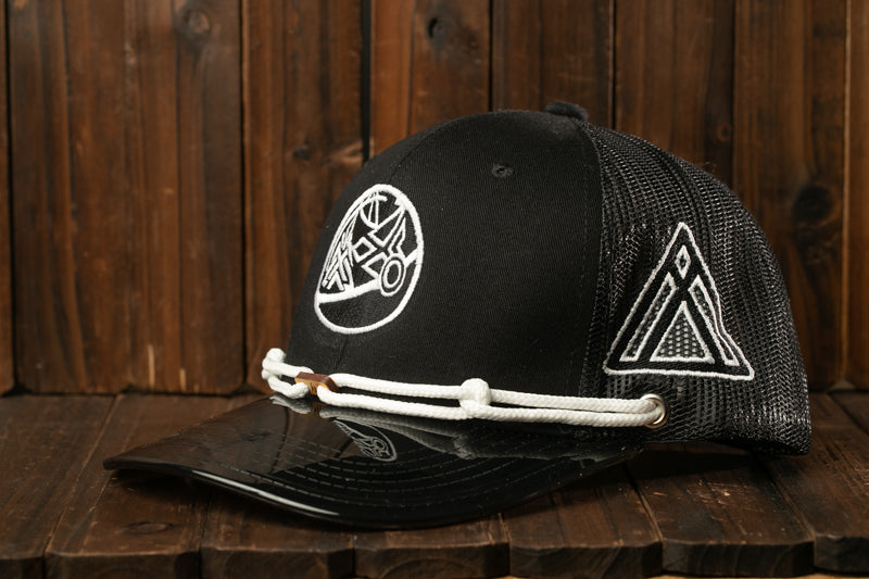 A black baseball cap with a mesh panel and a white logo on the front, resting on a wooden surface.
