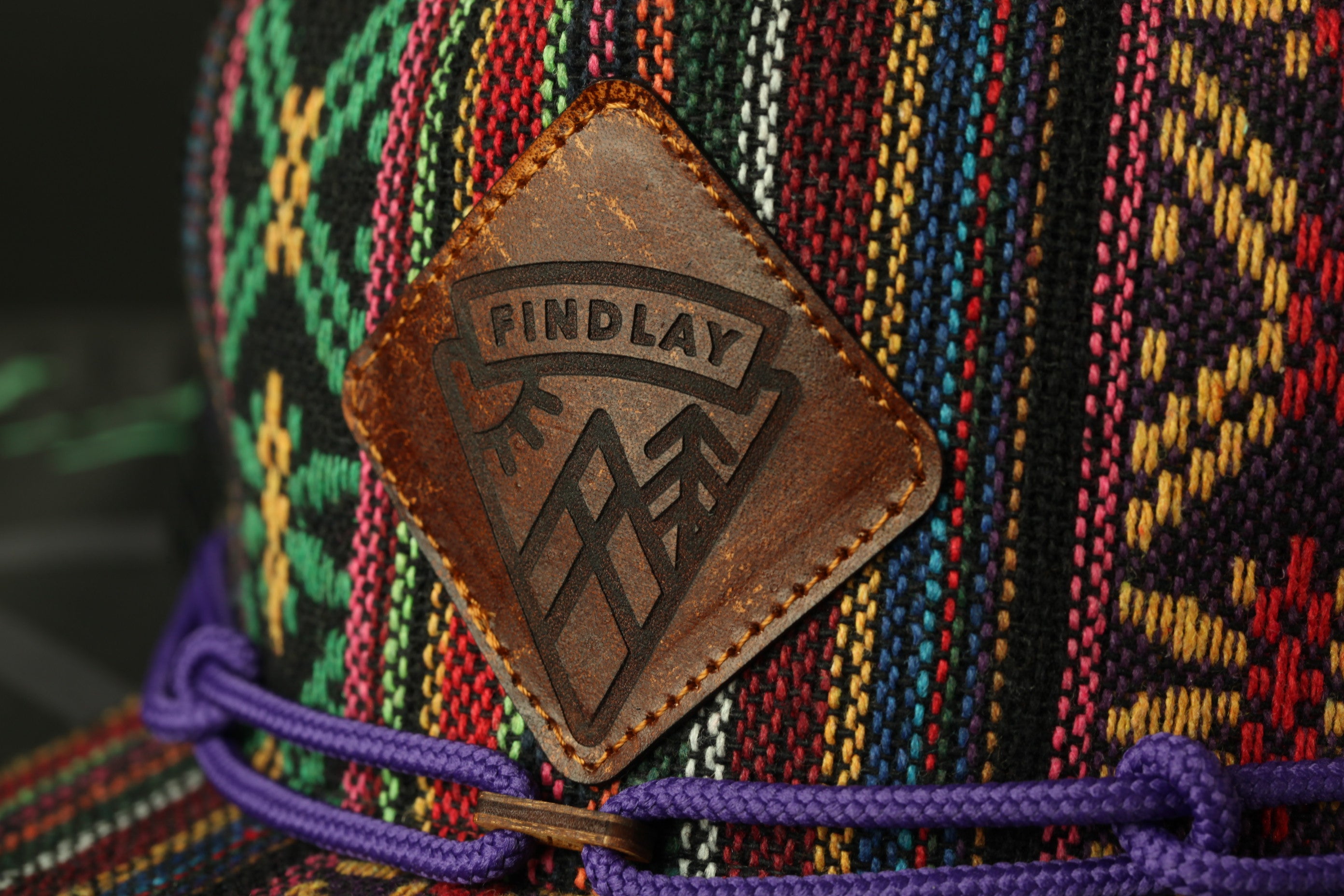 A close-up of a colorful, patterned hat with a leather patch featuring the word "FINDLAY" on it.