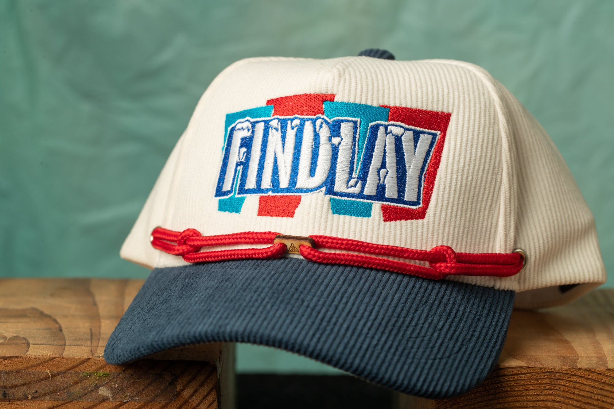 A white baseball cap with the word "FINDLAY" embroidered on it, sitting on a wooden surface.