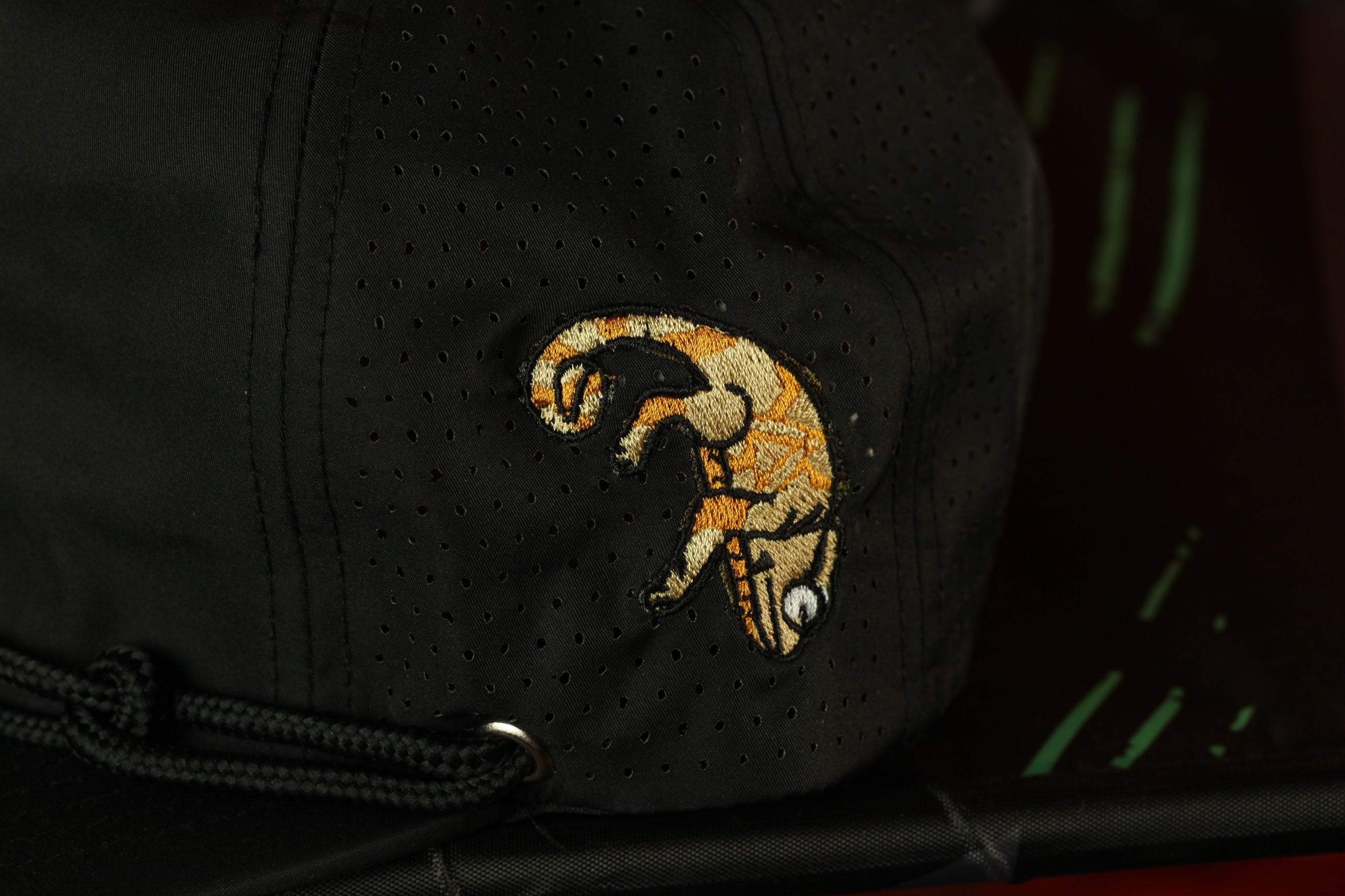 A close-up view of a black baseball cap with a detailed embroidered design on the front.