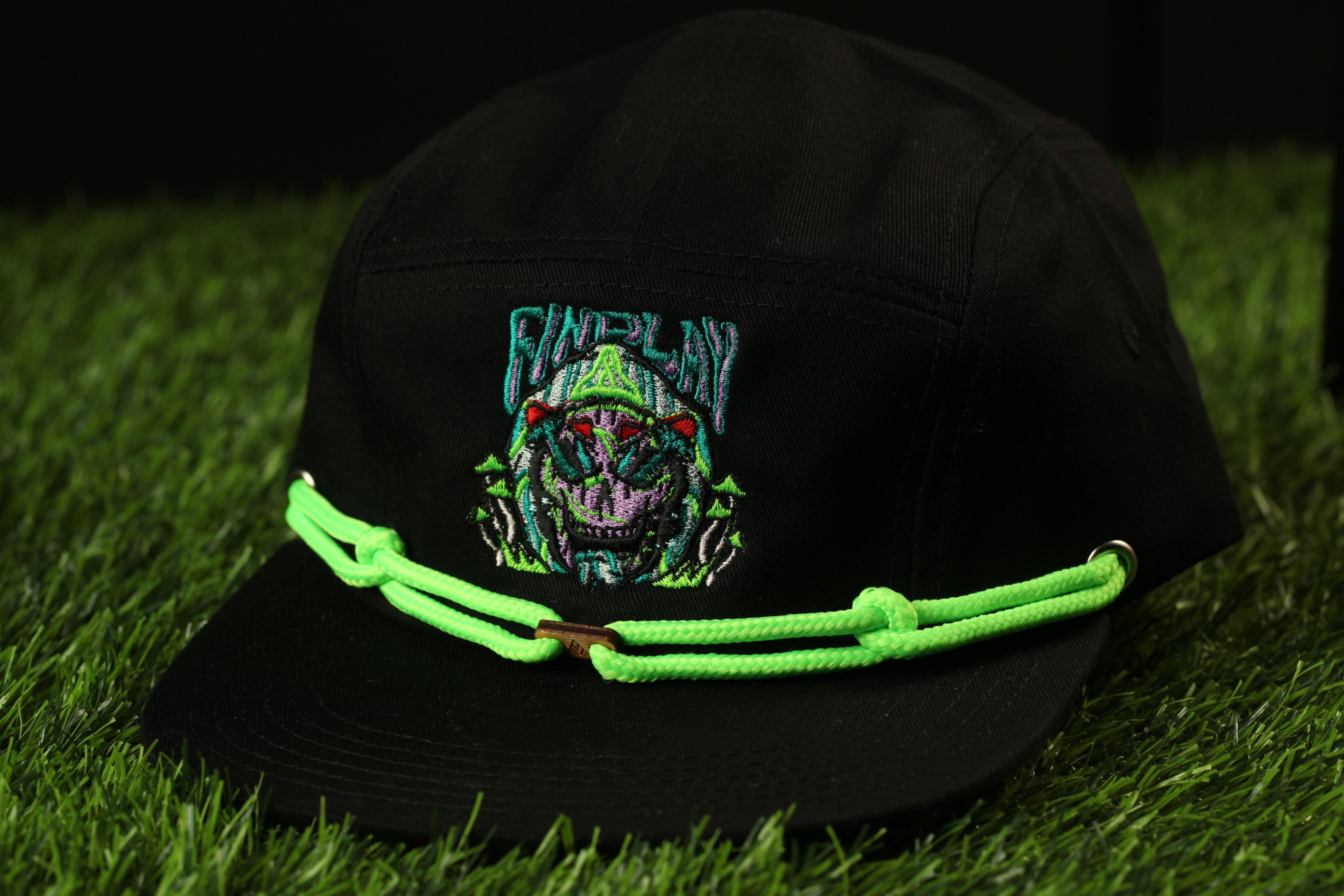 A black baseball cap with a green rope strap and a colorful graphic design on the front.