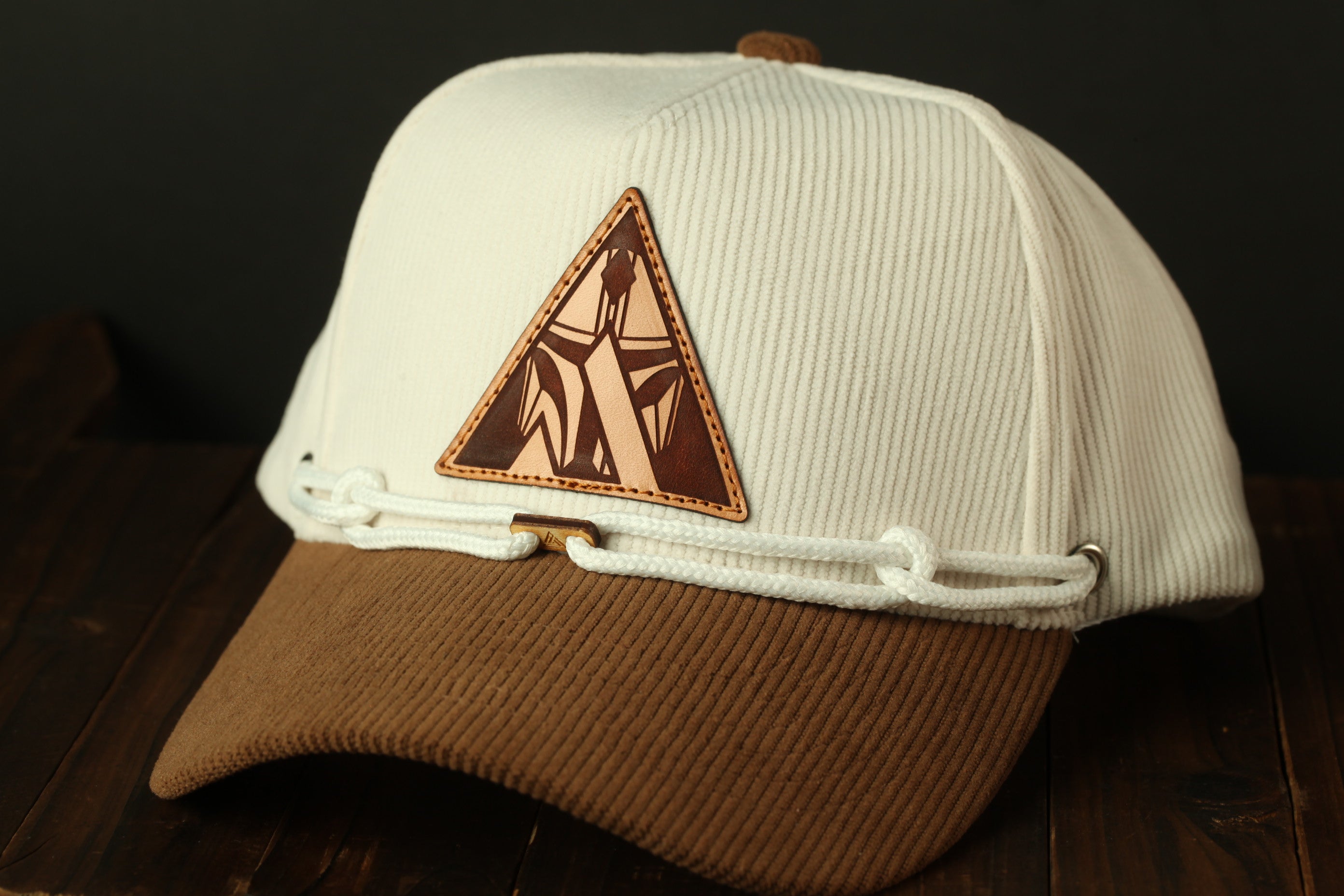 A white baseball cap with a brown leather patch on the front, placed on a wooden surface.