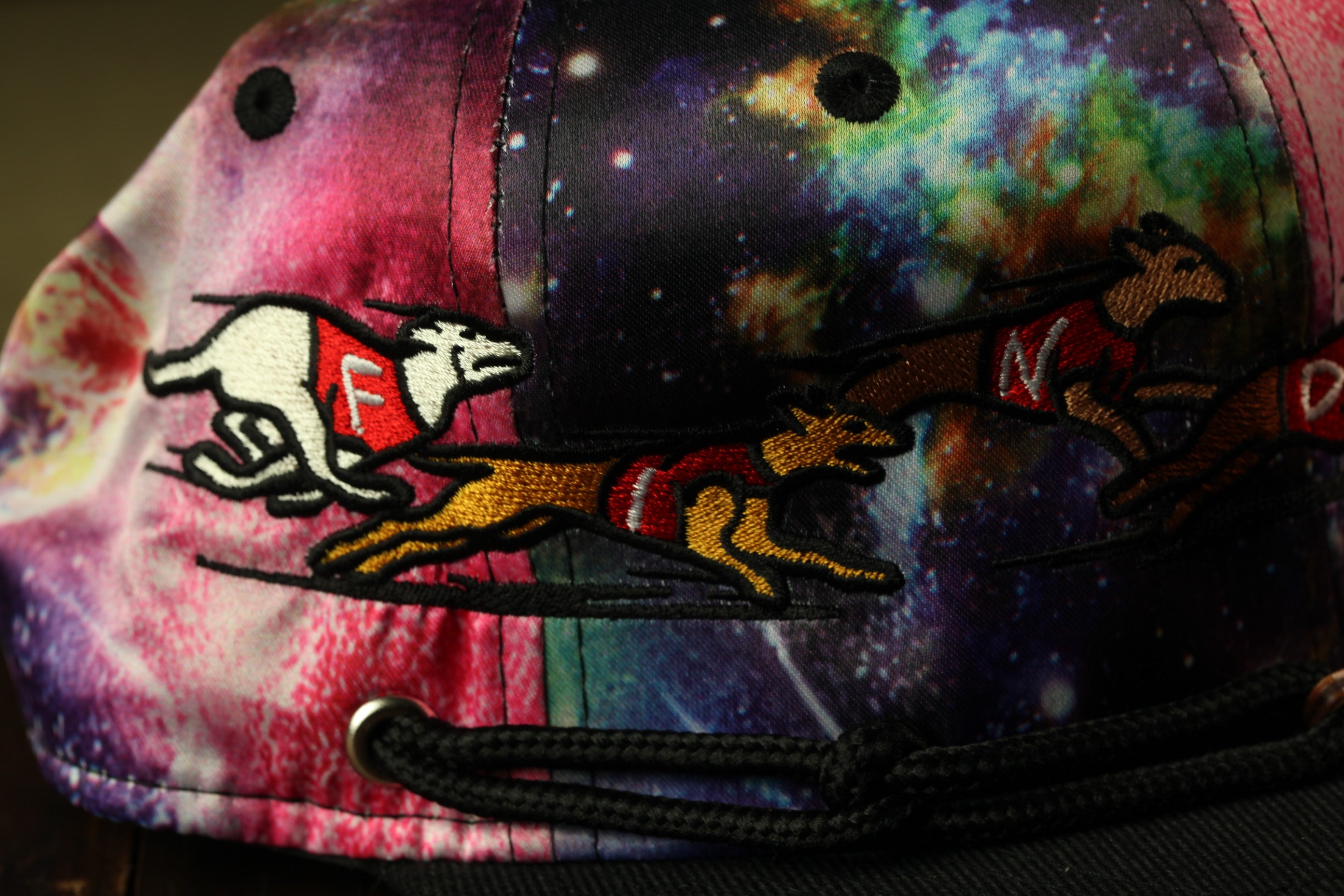 A colorful, patterned baseball cap with a design featuring a running dog and a racing dog on a cosmic background.