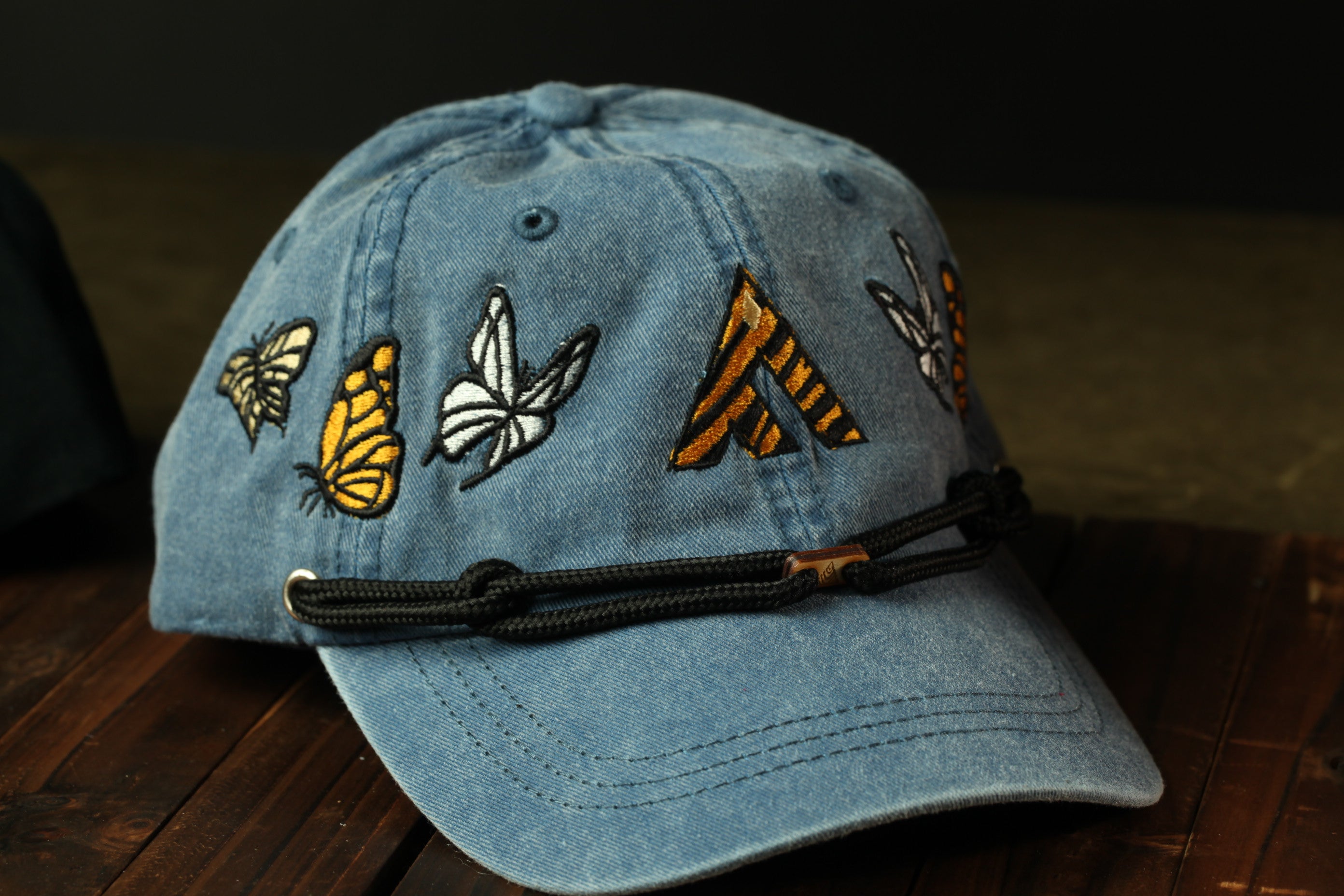 A blue baseball cap with embroidered butterflies and a triangular design on the front.