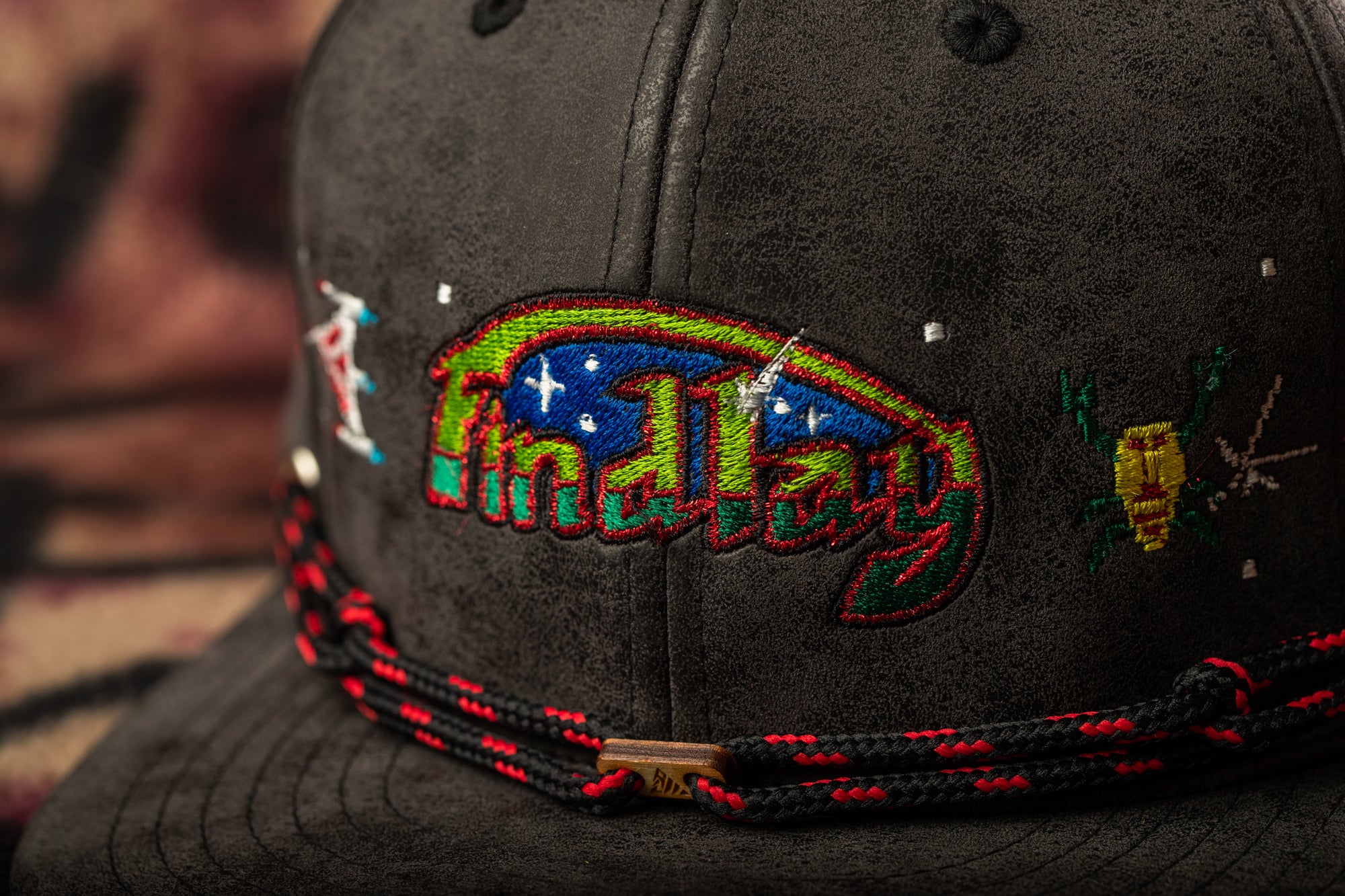 A close-up view of a black baseball cap with colorful embroidered designs, including a large "Findlay" logo and various other patterns.