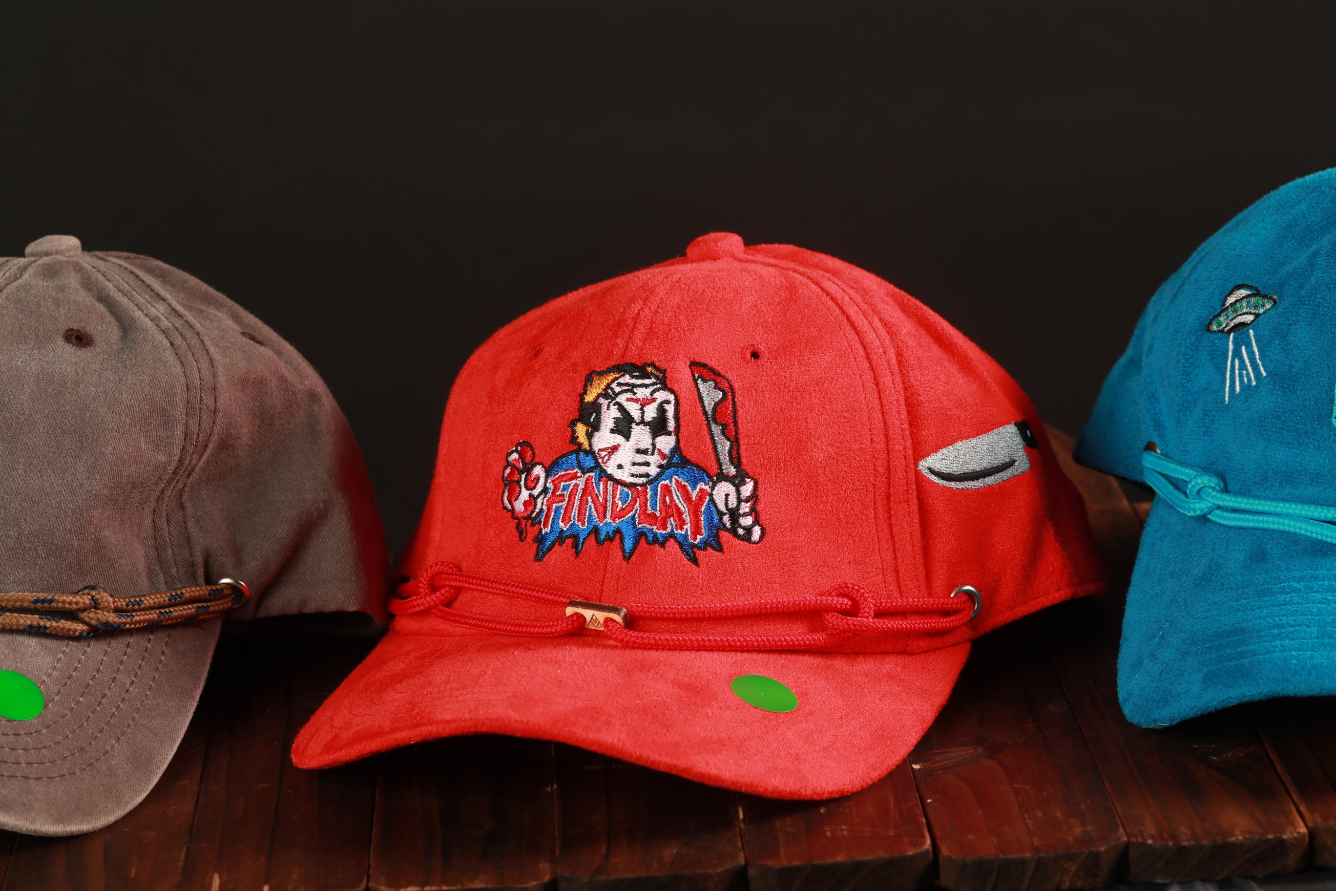 Three baseball caps are displayed on a wooden surface, each with a unique design and color.