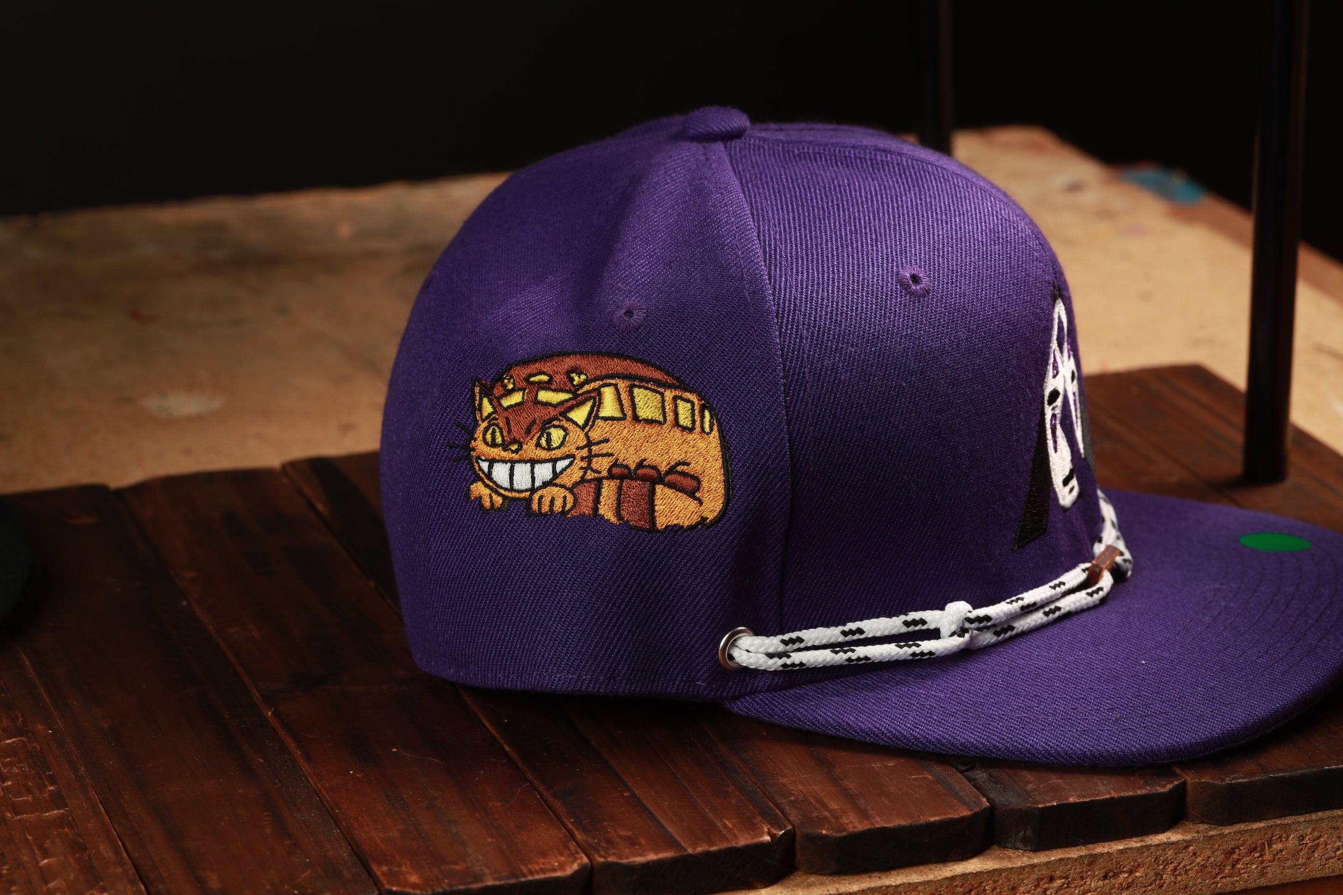 A purple baseball cap with a cat embroidered on it, sitting on a wooden surface.