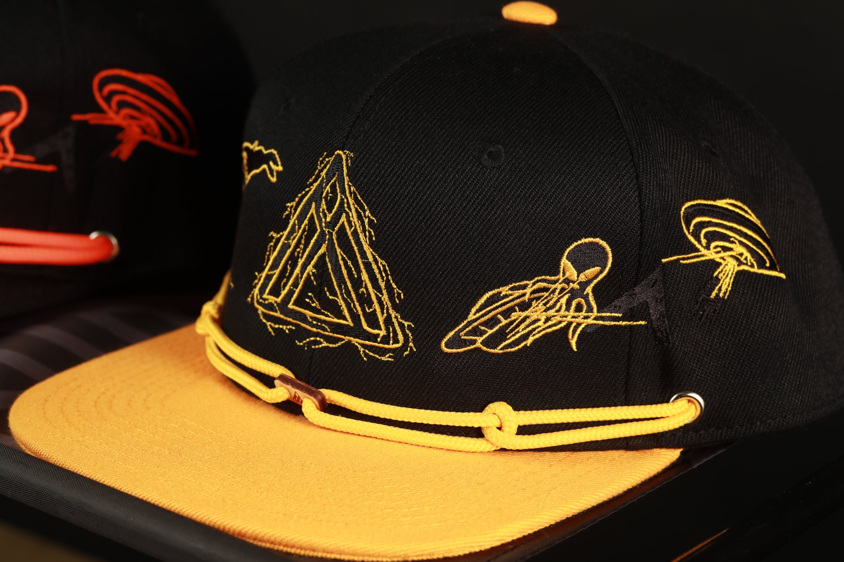 A close-up image of a black baseball cap with yellow accents, featuring various embroidered designs and patterns.