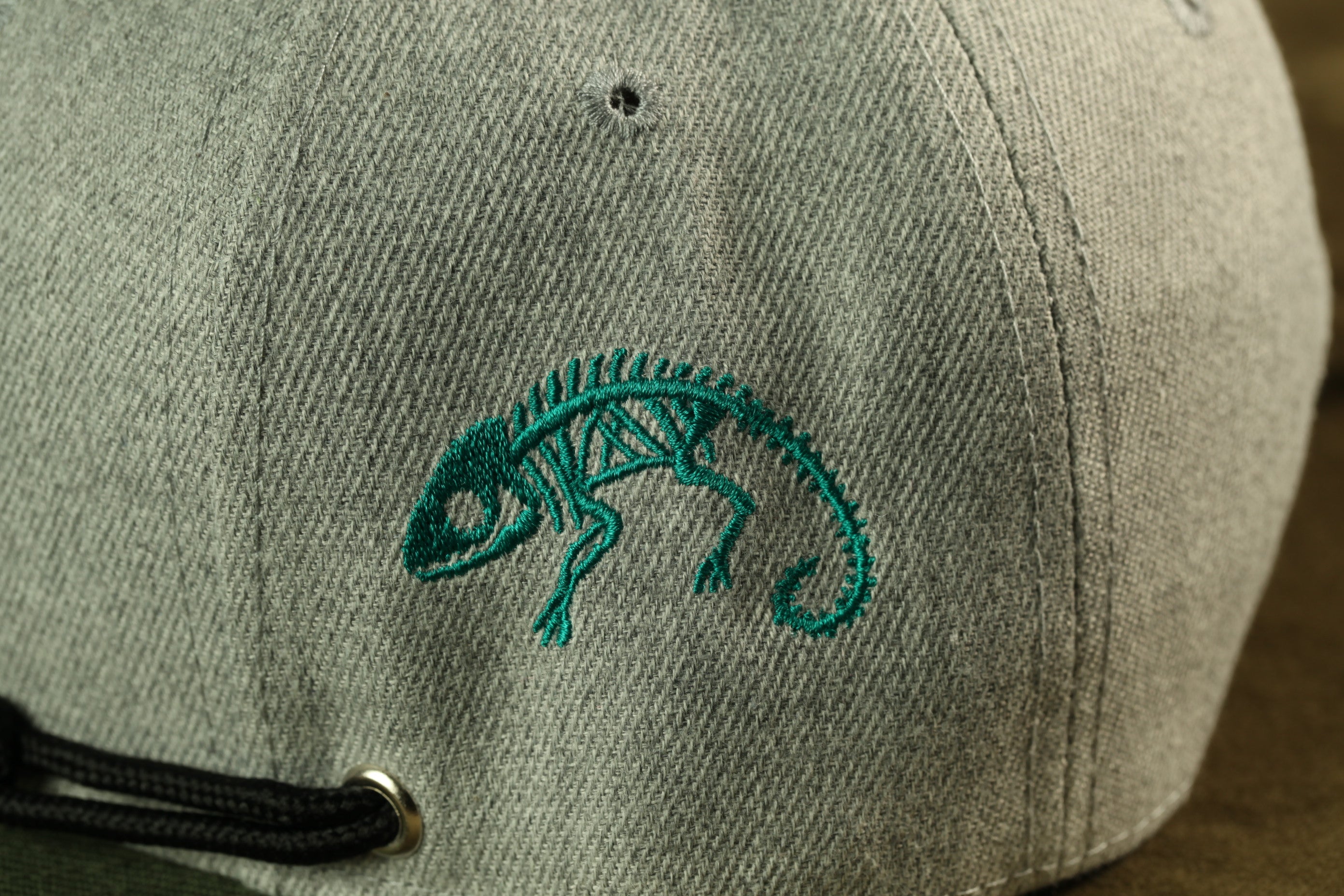 a close-up view of a gray baseball cap with a green chameleon embroidered on it.