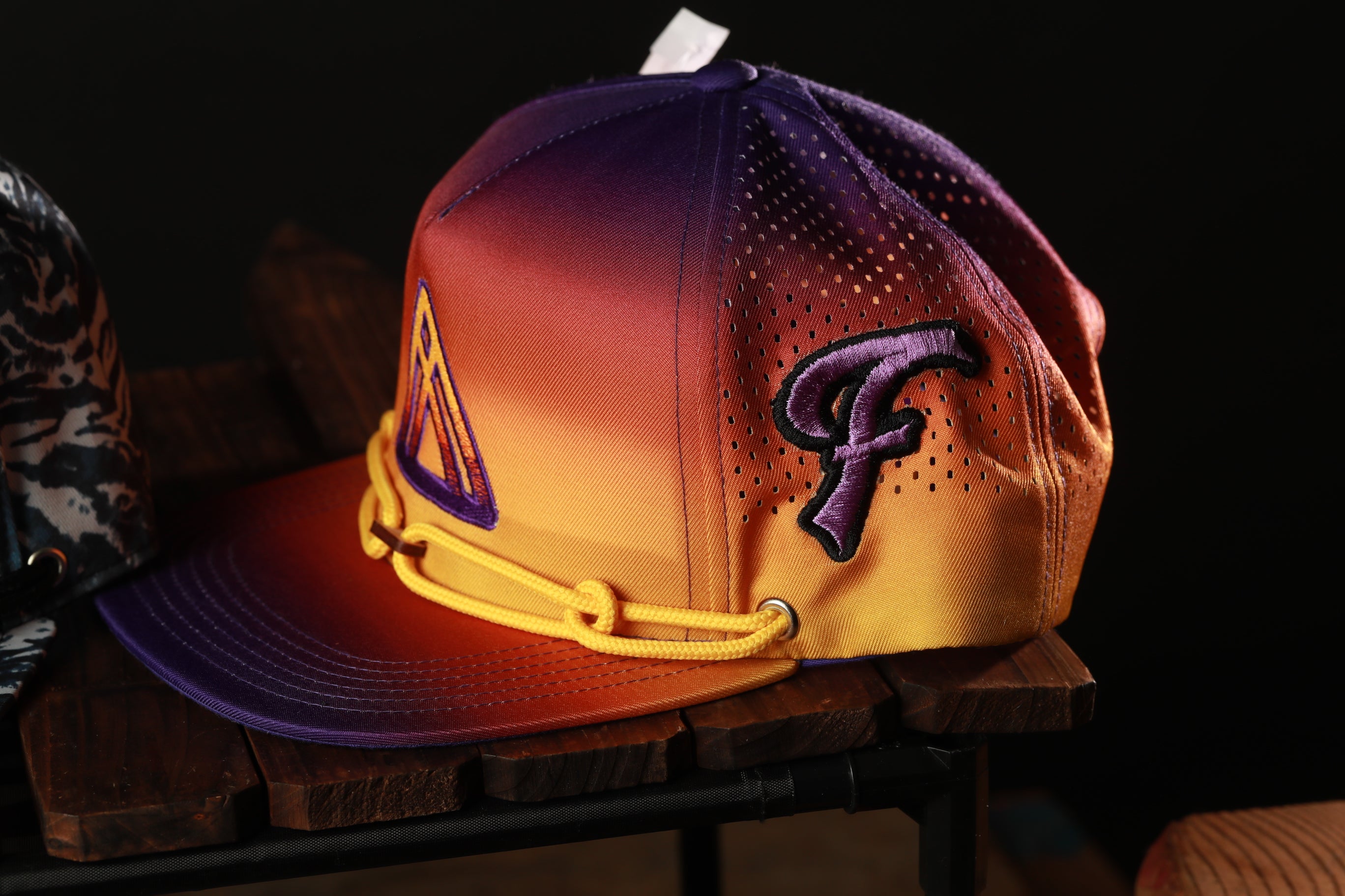 A colorful baseball cap with a purple and orange gradient design, featuring a prominent purple "P" logo, is displayed on a wooden surface.